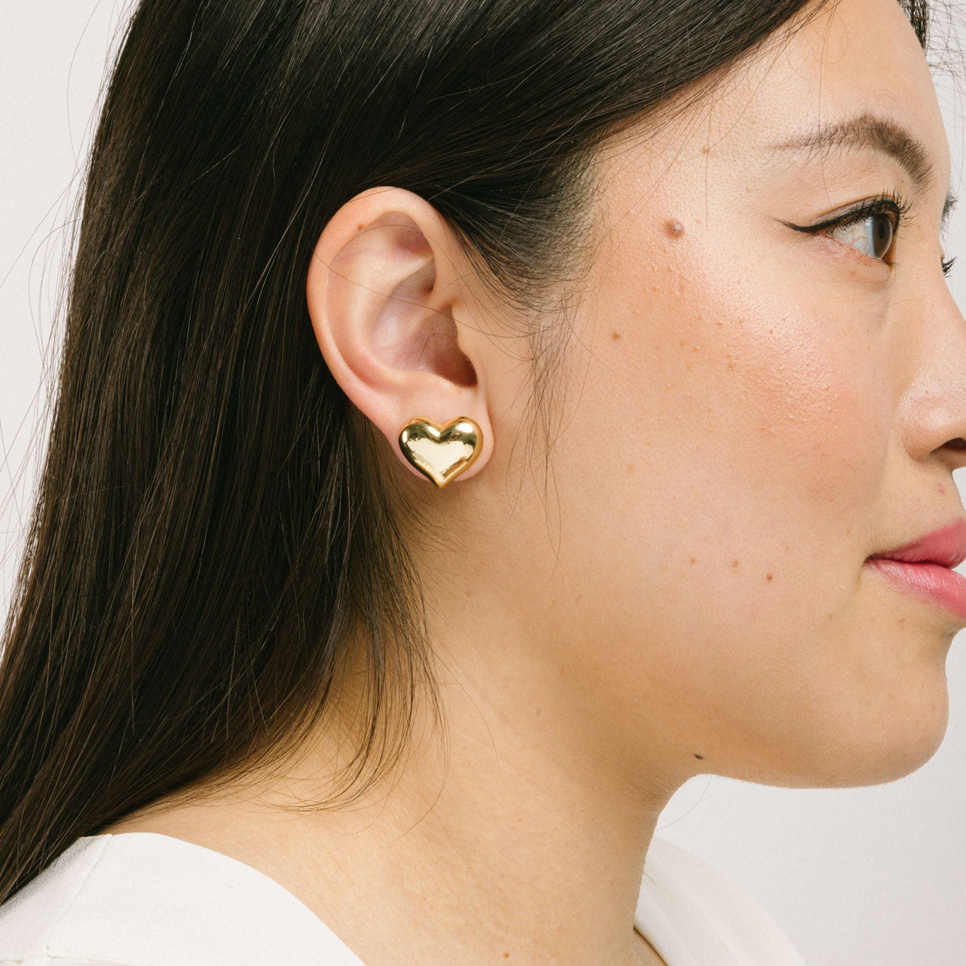 A model wearing the Coeur Clip On Earrings in Gold offer a medium-strength, adjustable hold via a mosquito coil clip. Ideal for all ear types, these earrings provide a secure yet comfortable fit for up to 24 hours. Crafted with Zinc Alloy and Copper, each purchase contains a single pair.