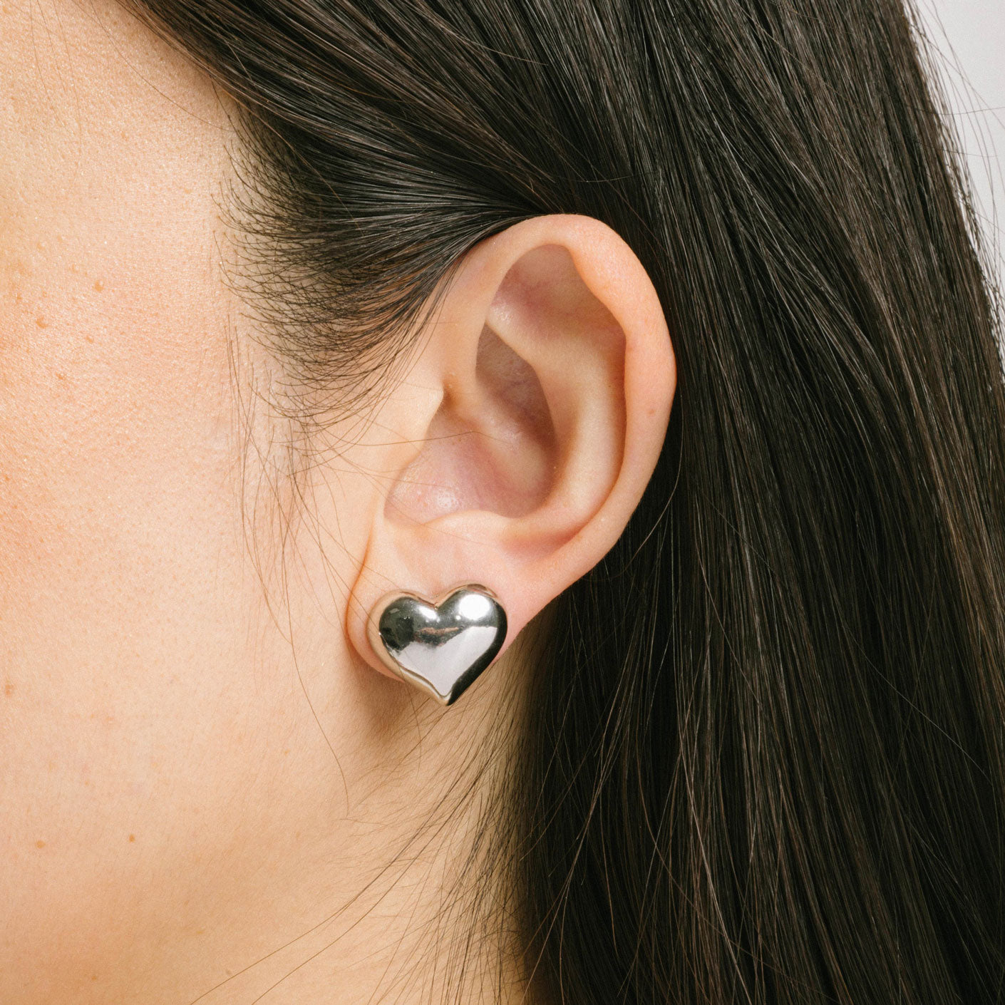 A model wearing the Coeur Clip On Earrings in Silver offer a medium-strength, adjustable hold via a mosquito coil clip. Ideal for all ear types, these earrings provide a secure yet comfortable fit for up to 24 hours. Crafted with Zinc Alloy and Copper, each purchase contains a single pair.