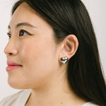 A model wearing the Coeur Clip On Earrings in Silver offer a medium-strength, adjustable hold via a mosquito coil clip. Ideal for all ear types, these earrings provide a secure yet comfortable fit for up to 24 hours. Crafted with Zinc Alloy and Copper, each purchase contains a single pair.
