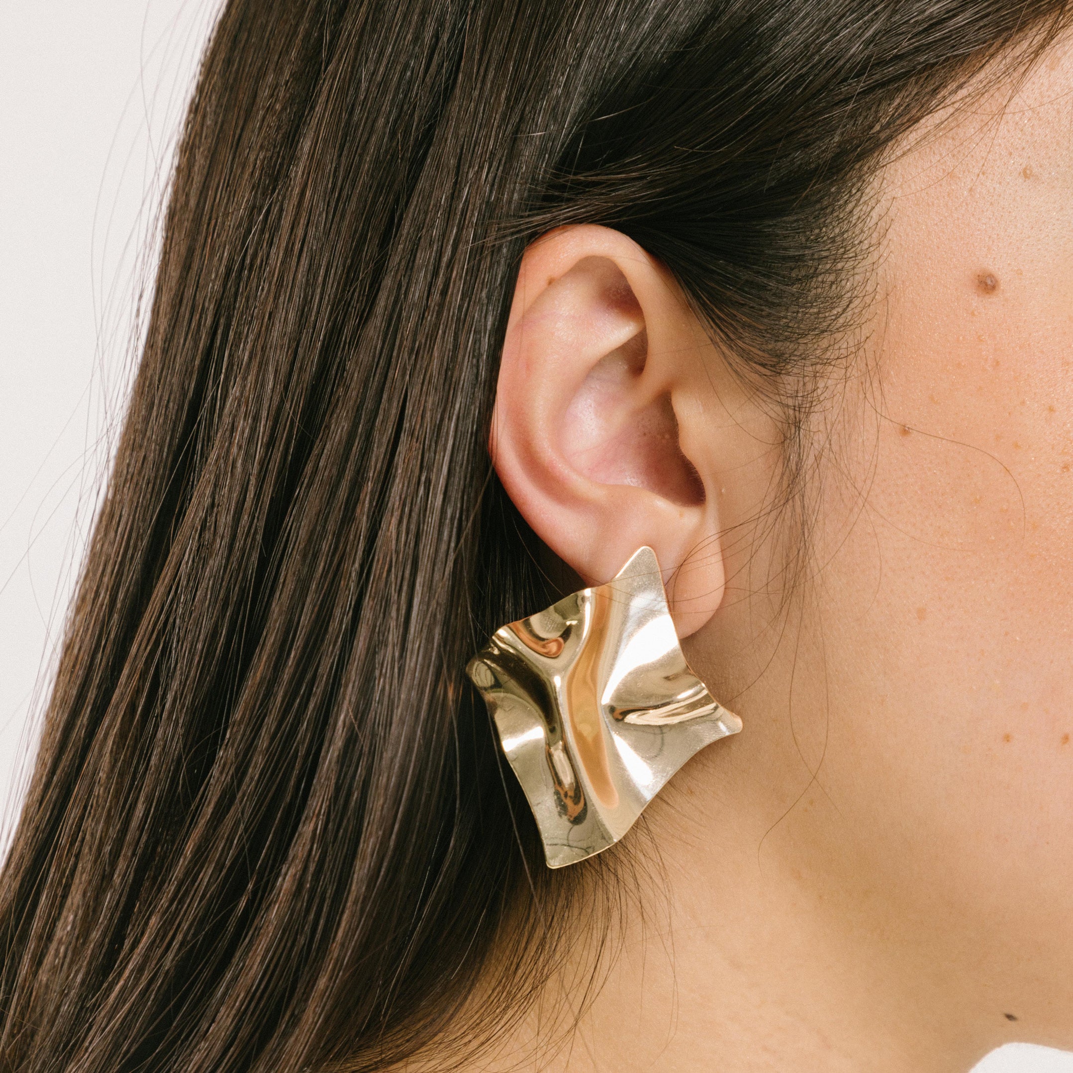 A model wearing the Crinkle Clip-On Earrings are fashioned from a gold-hued copper alloy and equipped with a removable rubber padding closure type; these earrings will imbue any woman's wardrobe with a fashionable flair.