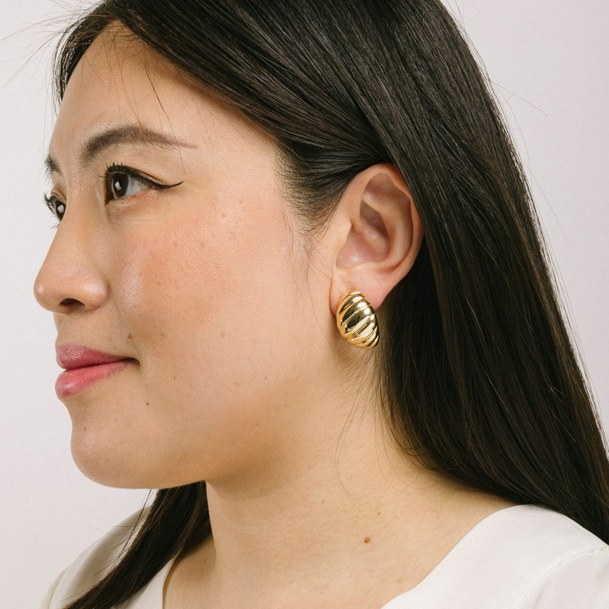 A model wearing the Croissant Dome Clip On Earrings in Gold are designed to provide a secure fit for all ear types. The rubber padding has a comfortable wear duration of 8-12 hours and is made with a Gold Tone Zinc Alloy. This item includes one pair.