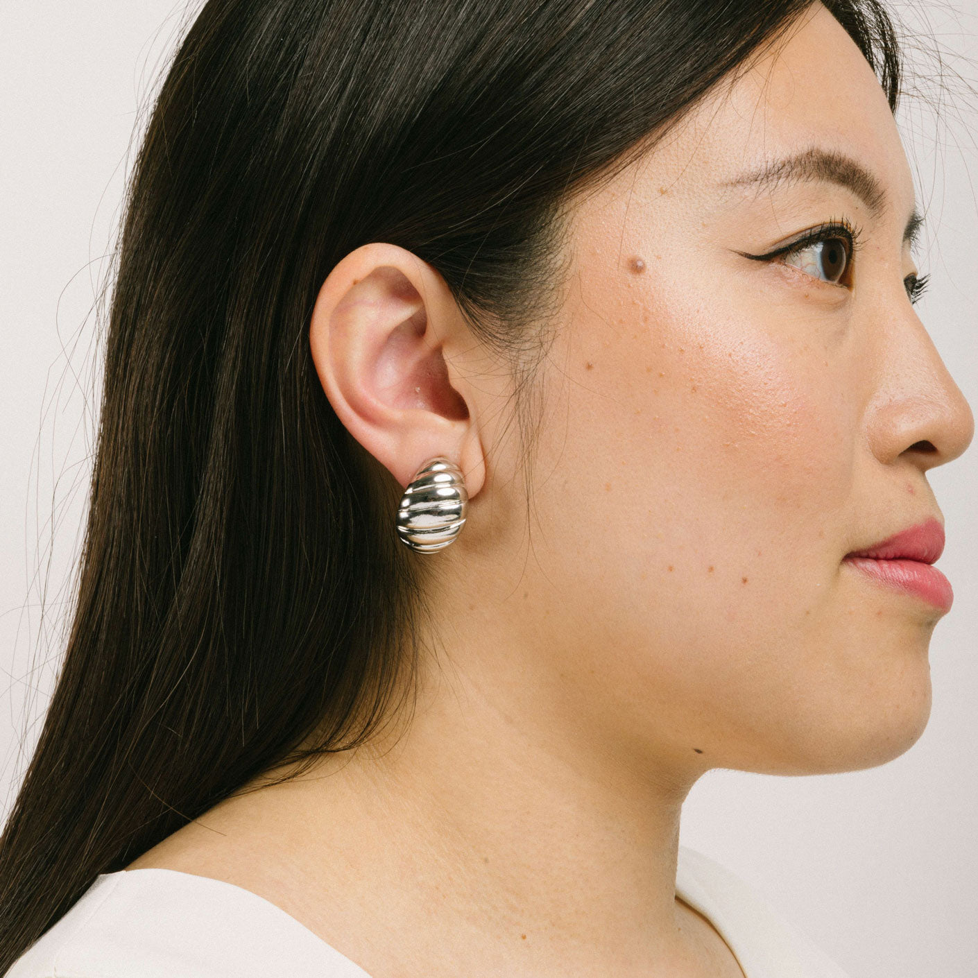 A model wearing the Croissant Dome Clip On Earrings in Silver are designed to provide a secure fit for all ear types. The rubber padding has a comfortable wear duration of 8-12 hours and is made with a Gold Tone Zinc Alloy. This item includes one pair.