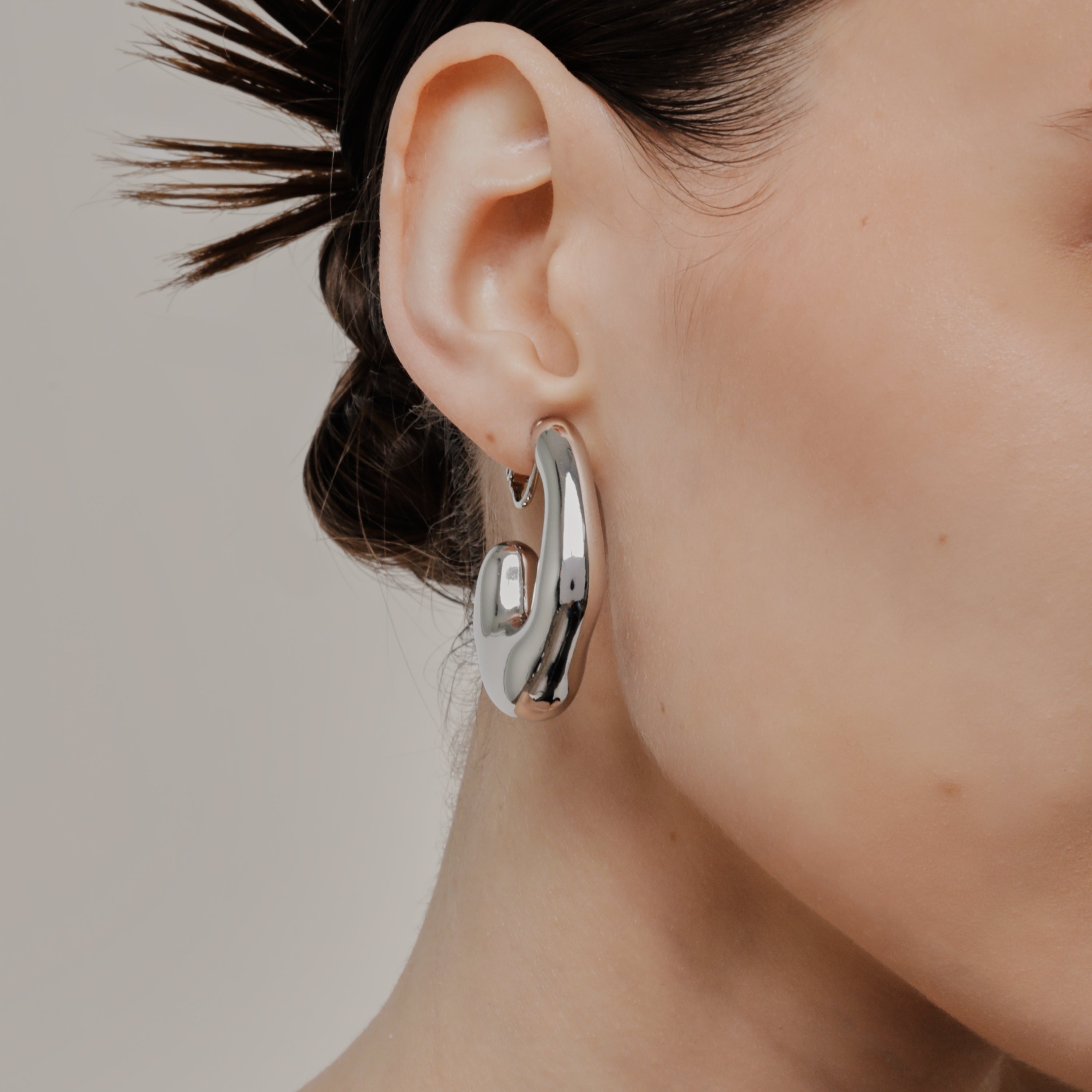 A model wearing the Curvy Hoop Clip On Earrings in Silver. These earrings offer comfort and versatility with a secure screwback closure that suits all ear sizes. Enjoy 8-12 hours of wear without discomfort, suitable for any ear type. Please note that each purchase includes one pair.