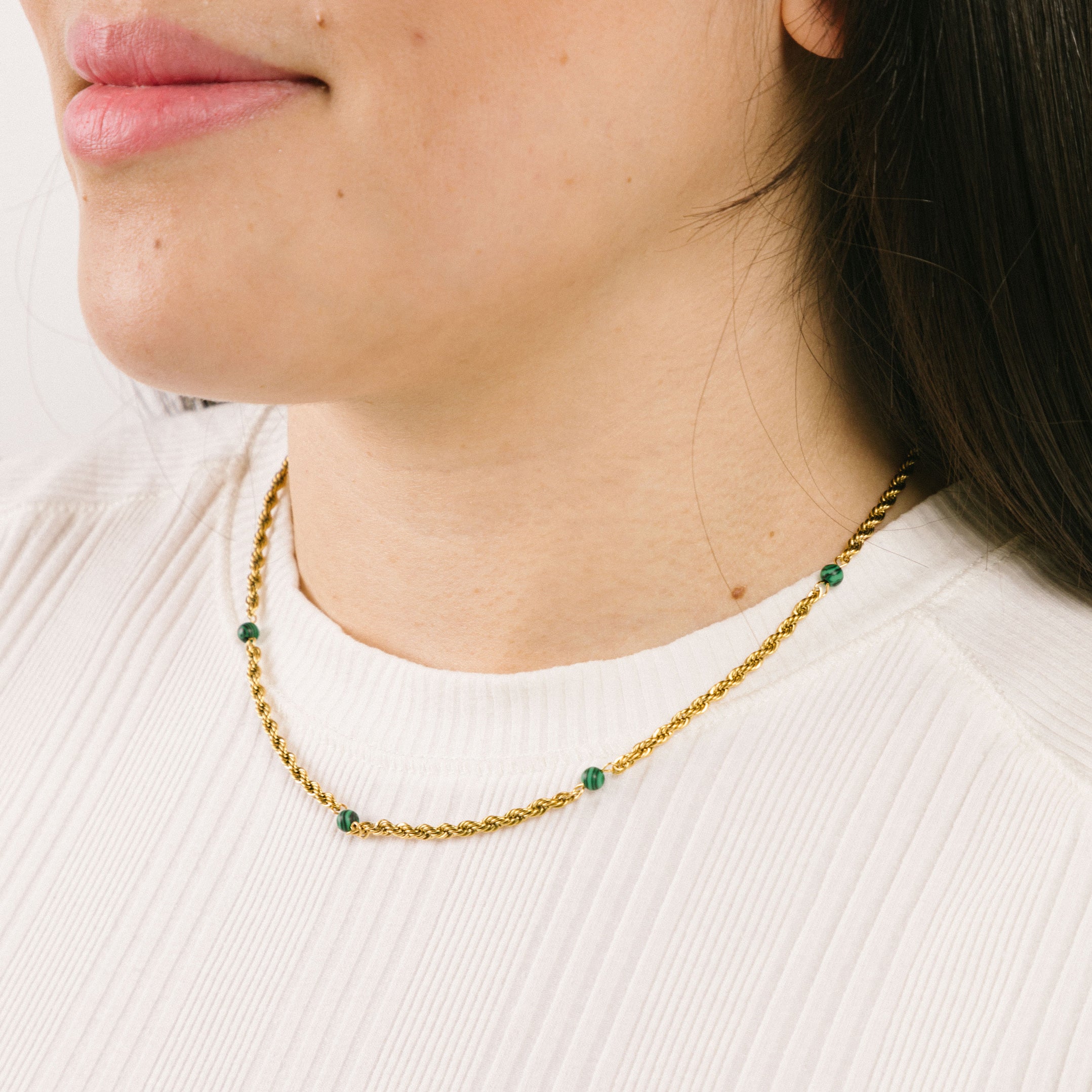 A model wearing the Cyrus Chain Necklace features adjustable sizing and is constructed with 18K gold-plated stainless steel and natural malachite stone for a durable, non-tarnish, and waterproof design. Please note that this item is one necklace.