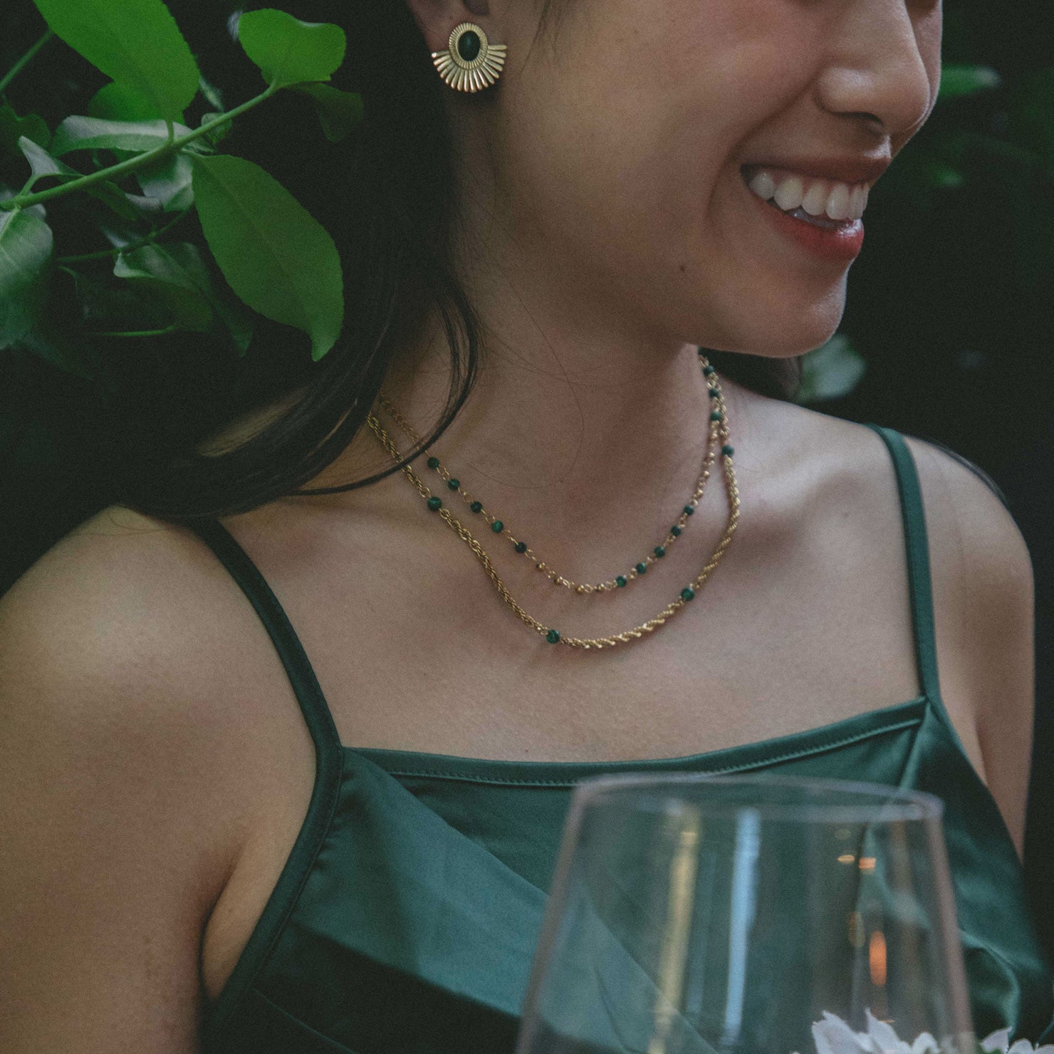 A model wearing the Cyrus Chain Necklace features adjustable sizing and is constructed with 18K gold-plated stainless steel and natural malachite stone for a durable, non-tarnish, and waterproof design. Please note that this item is one necklace.