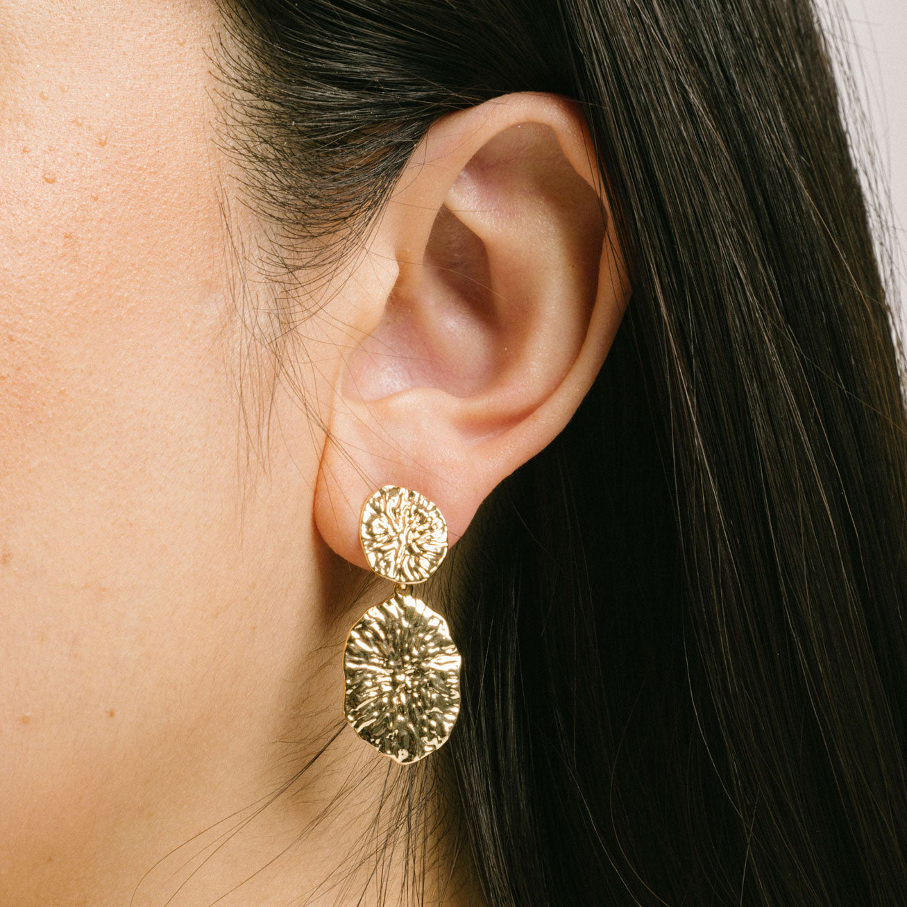 A model wearing the Daiquiri Drop Clip On Earrings in Gold feature a secure, padded clip-on closure ideal for all ear types, offering up to 12 hours of comfortable wear. Crafted from Zinc and Copper alloy, these earrings come as a single pair with removable rubber padding.