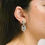 A model wearing the Daiquiri Drop Clip On Earrings in Silver feature a secure, padded clip-on closure ideal for all ear types, offering up to 12 hours of comfortable wear. Crafted from Zinc and Copper alloy, these earrings come as a single pair with removable rubber padding.