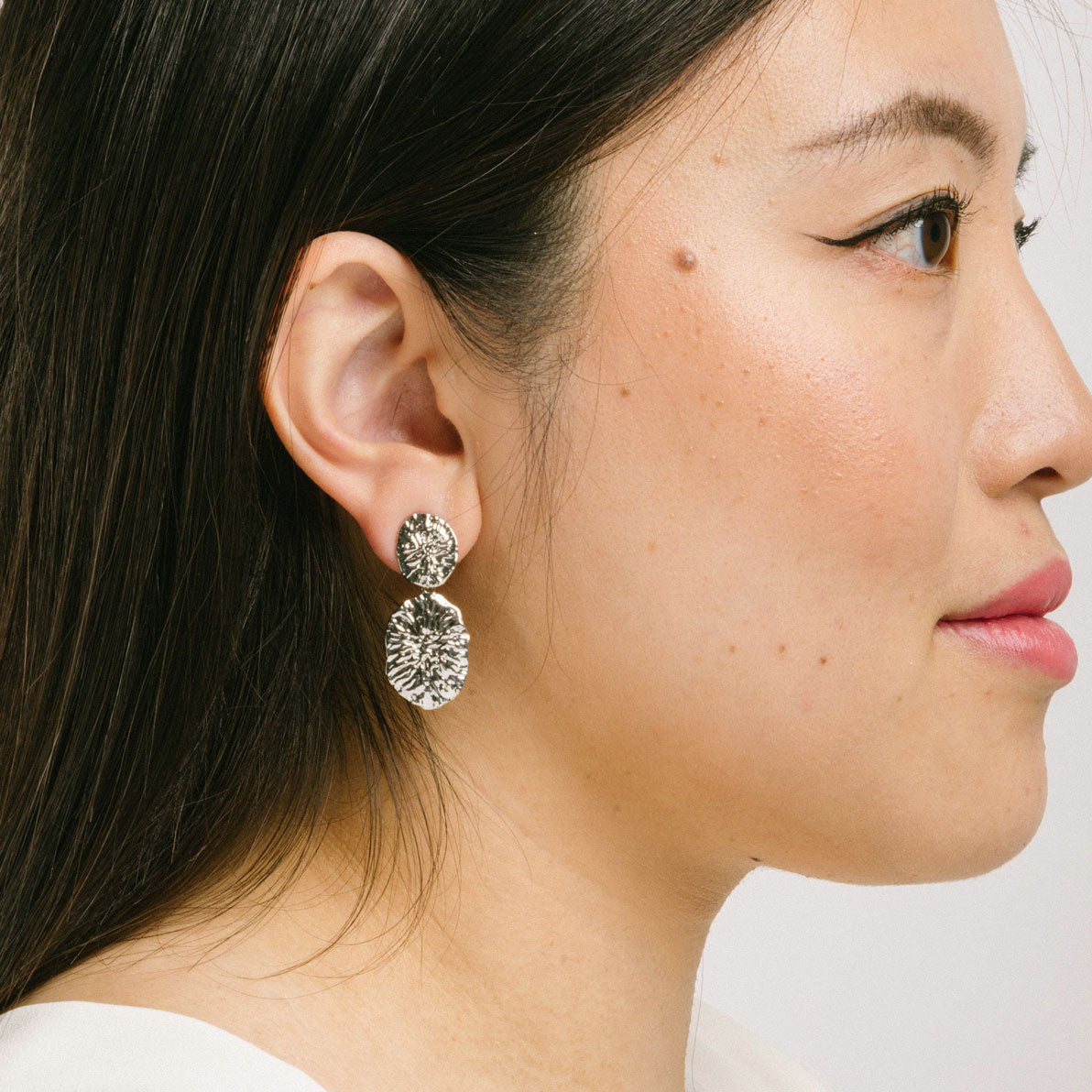 A model wearing the Daiquiri Drop Clip On Earrings in Silver feature a secure, padded clip-on closure ideal for all ear types, offering up to 12 hours of comfortable wear. Crafted from Zinc and Copper alloy, these earrings come as a single pair with removable rubber padding.