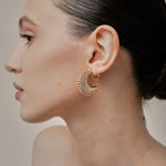 A model wearing the Deco Hoop Clip On Earrings in Gold. Designed with a screwback closure, these earrings provide a secure hold for all types of ears. Whether you have thick, sensitive, small, or keloid prone ears, these earrings can be manually adjusted to fit your size. Enjoy 8-12 hours of wear in these elegant, versatile earrings.