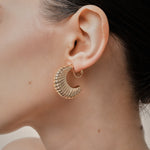 A model wearing the Deco Hoop Clip On Earrings in Gold. Designed with a screwback closure, these earrings provide a secure hold for all types of ears. Whether you have thick, sensitive, small, or keloid prone ears, these earrings can be manually adjusted to fit your size. Enjoy 8-12 hours of wear in these elegant, versatile earrings.