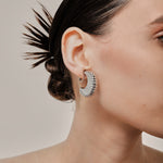 A model wearing the Deco Hoop Clip On Earrings in Silver. Designed with a screwback closure, these earrings provide a secure hold for all types of ears. Whether you have thick, sensitive, small, or keloid prone ears, these earrings can be manually adjusted to fit your size. Enjoy 8-12 hours of wear in these elegant, versatile earrings.