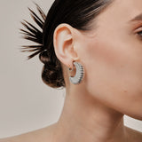 A model wearing the Deco Hoop Clip On Earrings in Silver. Designed with a screwback closure, these earrings provide a secure hold for all types of ears. Whether you have thick, sensitive, small, or keloid prone ears, these earrings can be manually adjusted to fit your size. Enjoy 8-12 hours of wear in these elegant, versatile earrings.