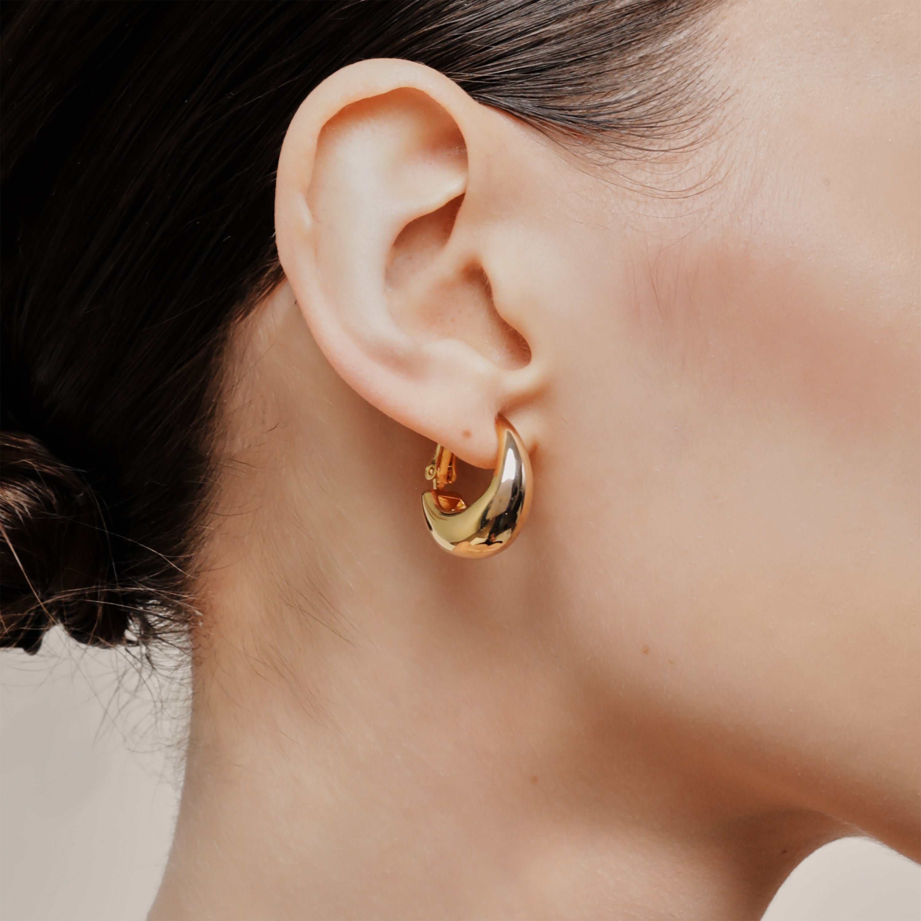 A model wearing the Dome Hoop Clip On Earrings in Gold. Adjustable for various ear types, including sensitive or stretched ears. Comes with a Mosquito Coil Clip-On Closure for a medium secure hold. Sold in pairs for a complete look.
