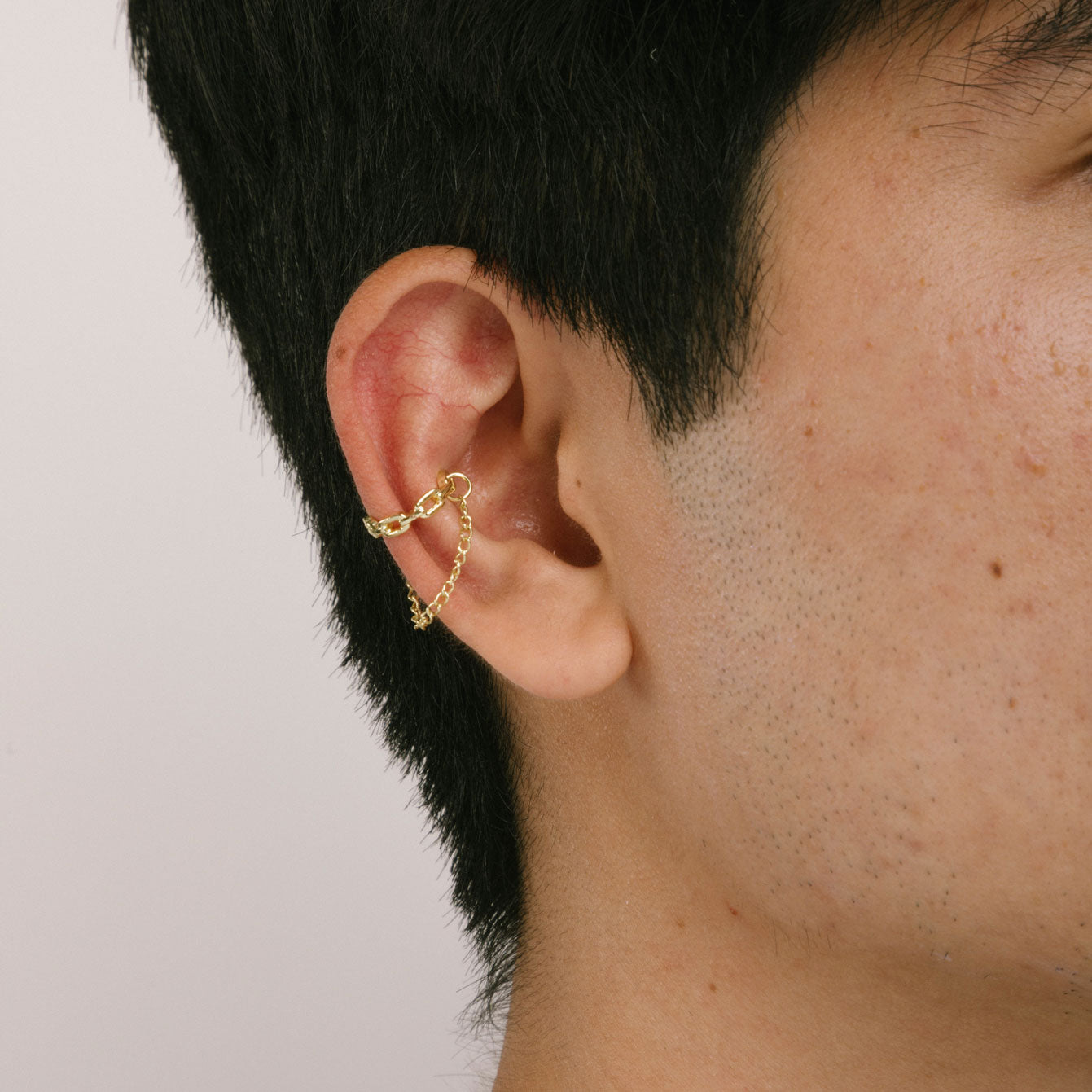 A model wearing the Double Chain Ear Cuff in Gold features a clip-on closure type that is suitable for all ear types, including thick/large ears, sensitive ears, small/thin ears and stretched/healing ears. On average, it allows for comfortable wear duration of up to 24 hours, providing a medium secure hold that can be adjusted if gently squeezed. Made of goldtone plated zinc alloy, the item is sold as one piece.