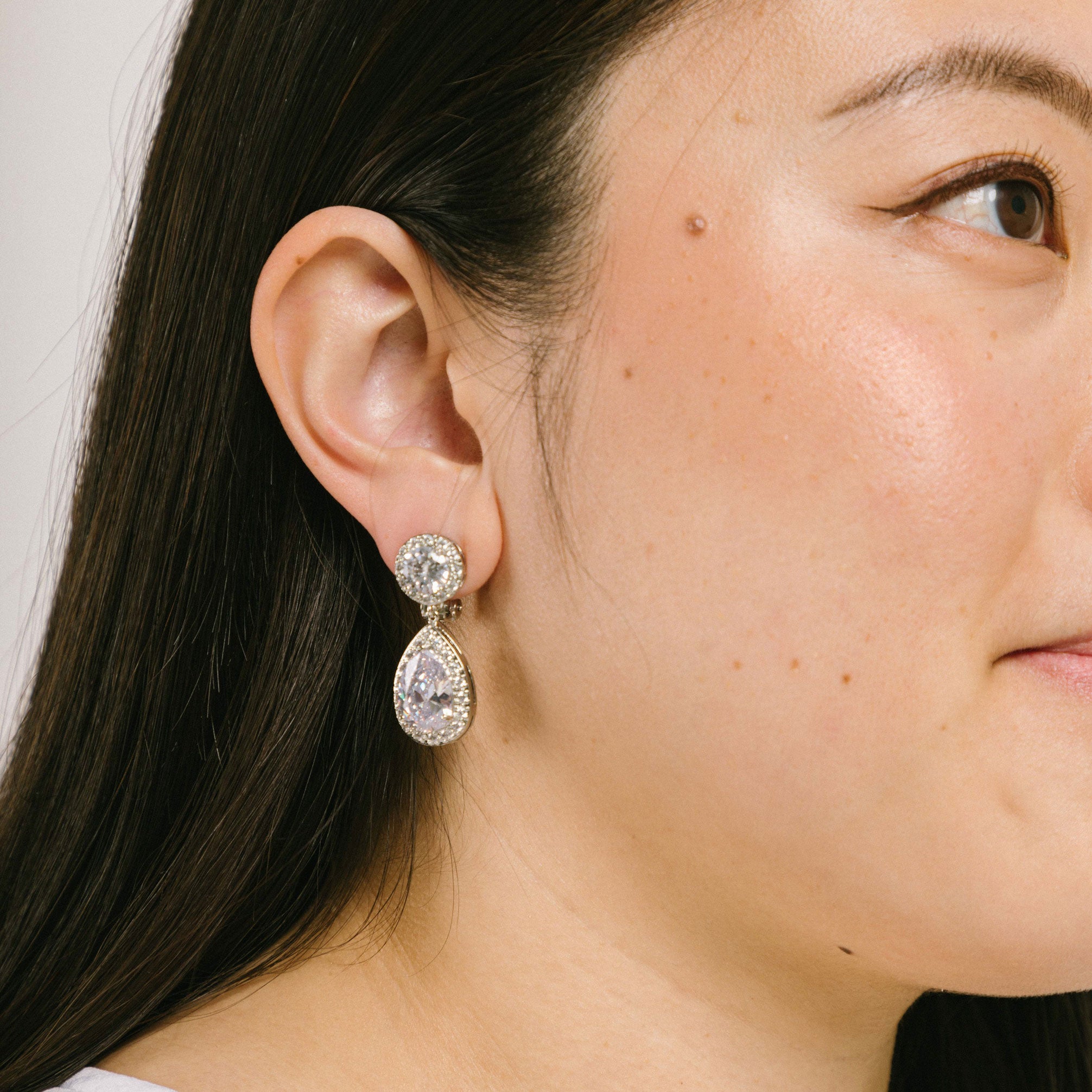 A model wearing the Eleanor Clip-On Earrings include a padded clip-on closure, secure hold, and long wear duration. This single pair of earrings is made of silver plated copper alloy and Cubic Zirconia, and is free from Lead, Nickel, and Cadmium. The adjustable rubber padding is removable.