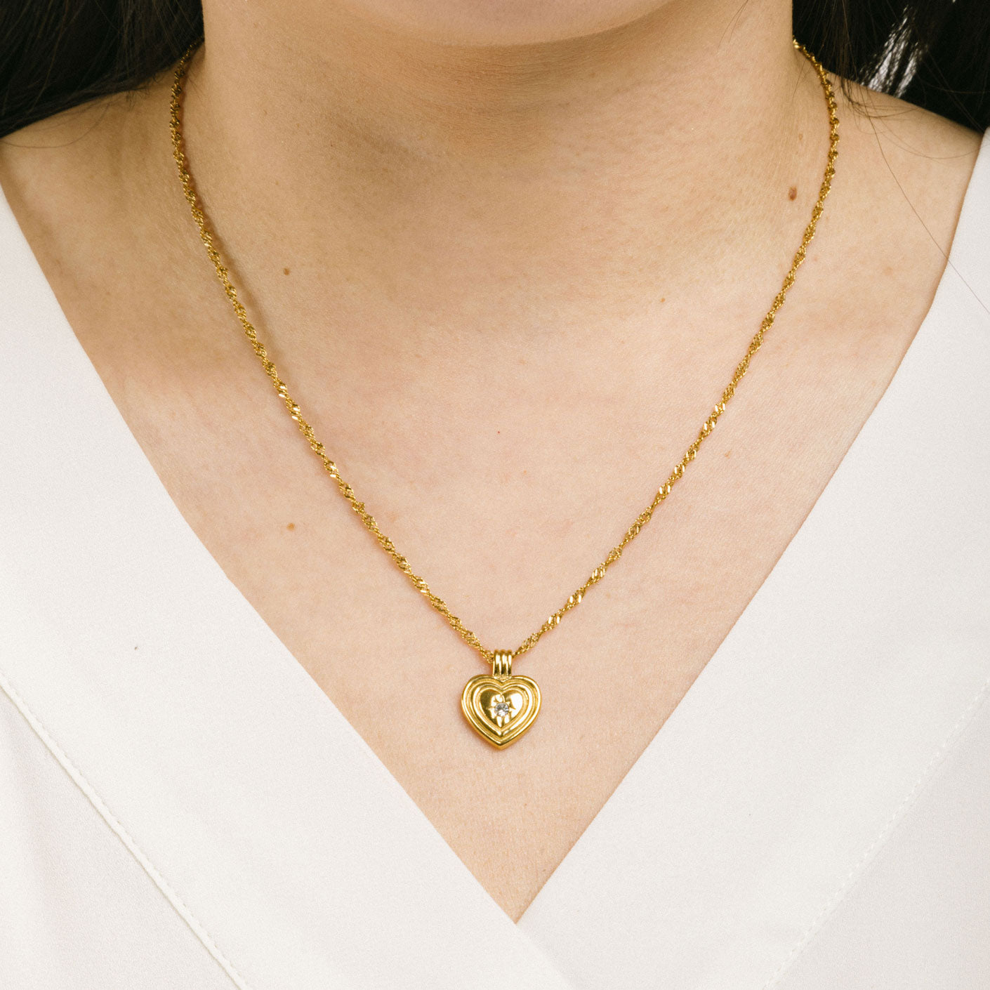 A model wearing the Ellie Heart Pendant Necklace is crafted from 14K Gold Plated Stainless Steel and embellished with Cubic Zirconia. It is adjustable and non-tarnish with great water and allergy resistance.