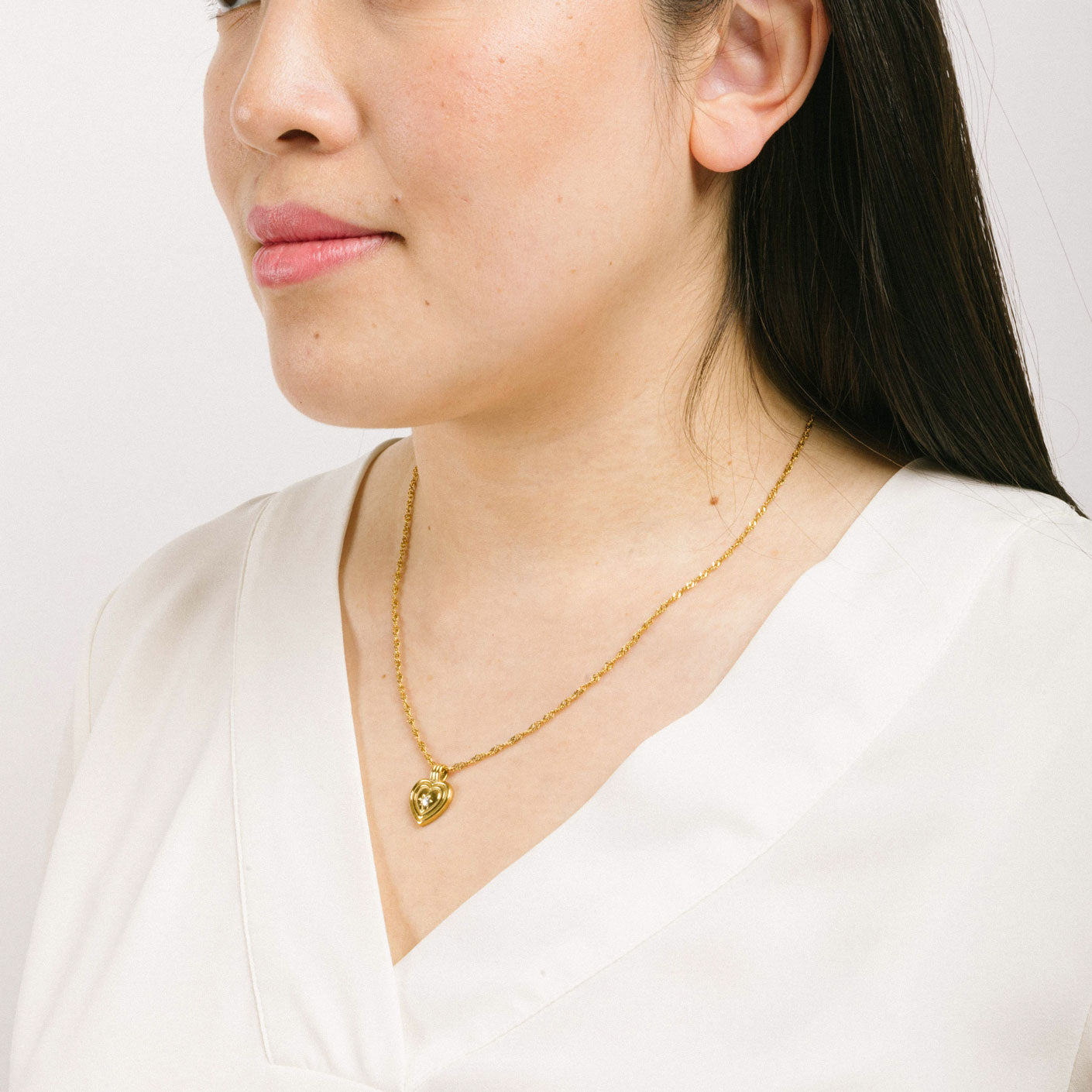 A model wearing the Ellie Heart Pendant Necklace is crafted from 14K Gold Plated Stainless Steel and embellished with Cubic Zirconia. It is adjustable and non-tarnish with great water and allergy resistance.