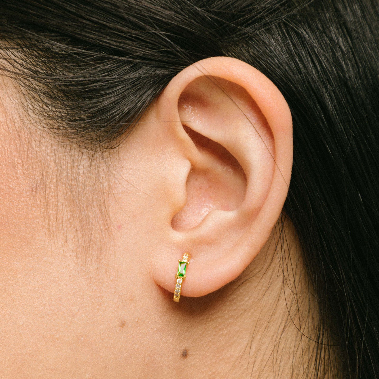 A model wearing the Emerald Pavé Huggie Clip-On Earrings features a closure type of mosquito coil clip-on earrings. They are suitable for all types of ear shapes and sizes, and are comfortable to wear for up to 24 hours. The hold strength is medium, allowing you to gently adjust the padding forward once on the ear. Crafted with 18k gold plated metal alloy and cubic zirconia, these earrings are non-tarnish and water-resistant.