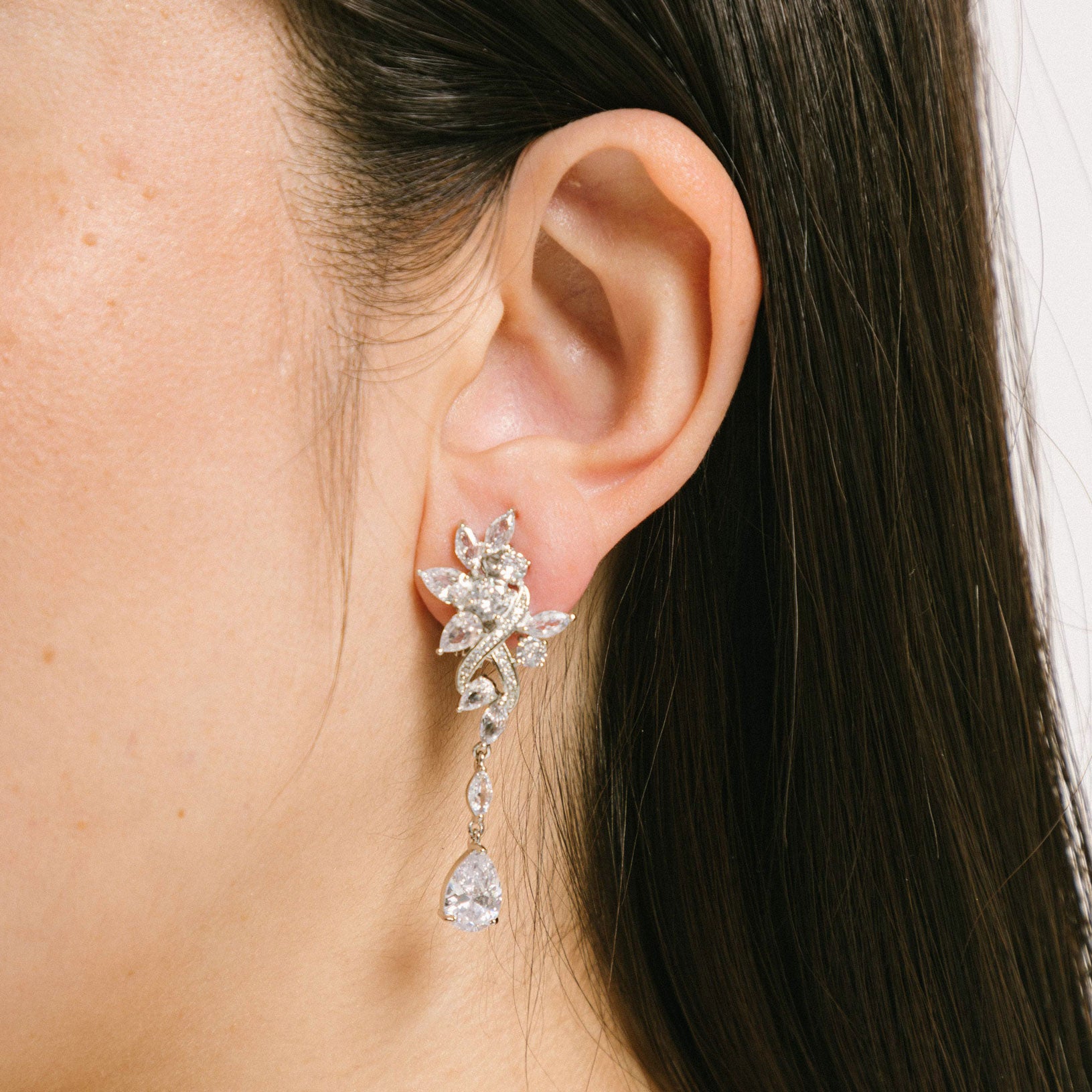 A model wearing the Evelyn Clip-On Earrings offer a secure fit for all ear types, ranging from thick/large ears to small/thin ears. With an average comfortable wear duration of 8-12 hours, these earrings have silver plated copper alloy components and feature a cubic zirconia setting. Additionally, the rubber padding is removable. Please note that this item is one pair.