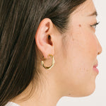 A model wearing the Twist Hoop Earrings feature a secure and comfortable screwback clip-on closure ideal for all ear types. Wear these earrings for up to 8-12 hours per day with a secure hold and the ability to be manually adjusted to the individual's size. Crafted from gold tone plated copper alloy, these earrings come is a single pair.