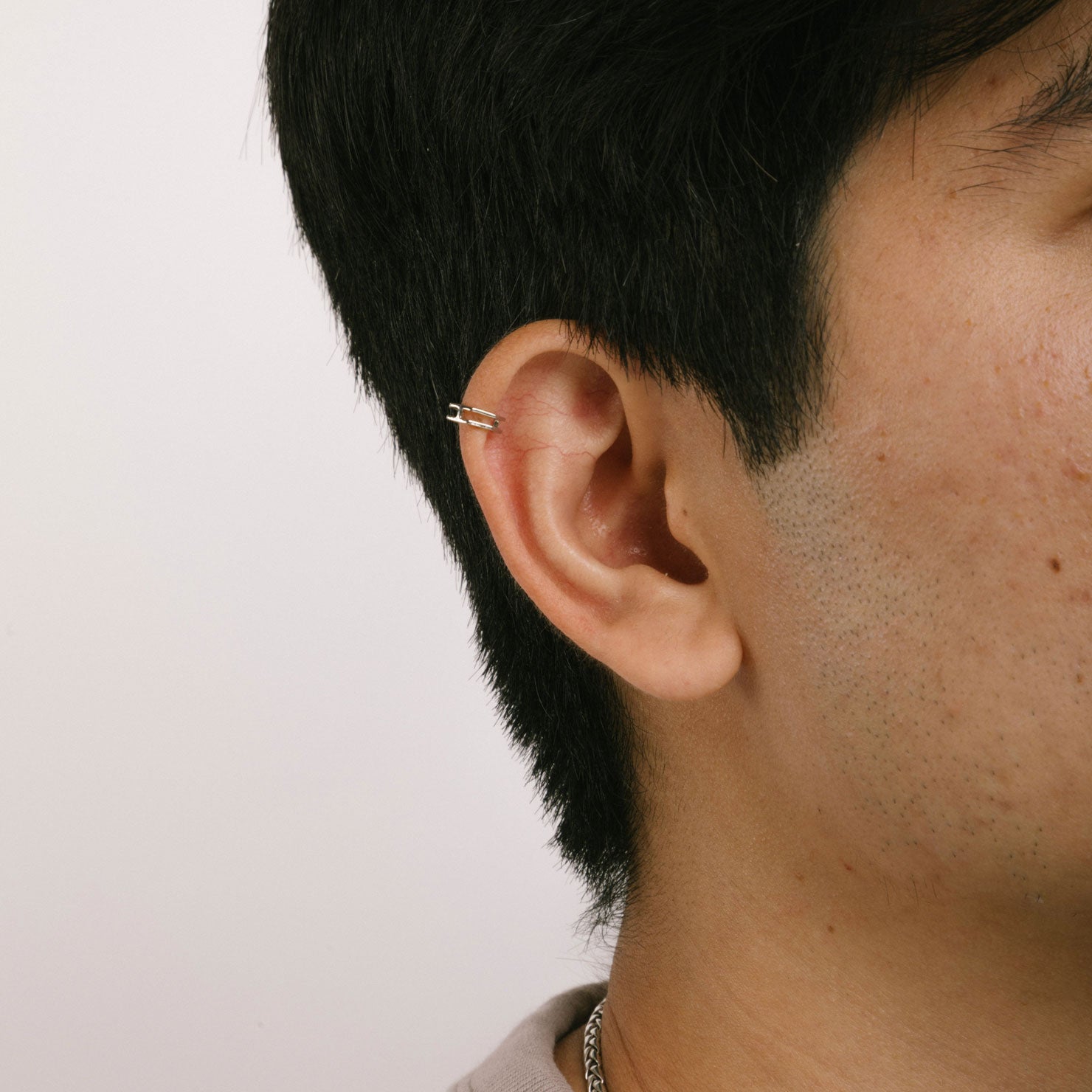 A model wearing the Heptagon Ear Cuff is a clip-on earring designed to fit all ear types, including thick/large, sensitive, small/thin, and stretched/healing ears. It offers a secure, medium hold that can be adjusted by gently squeezing the cuff once placed on the ear. This item is single-piece and is intended to be worn on the helix of the ear. Made from silver tone plated copper, this earring offers up to 24 hours of comfortable wear.