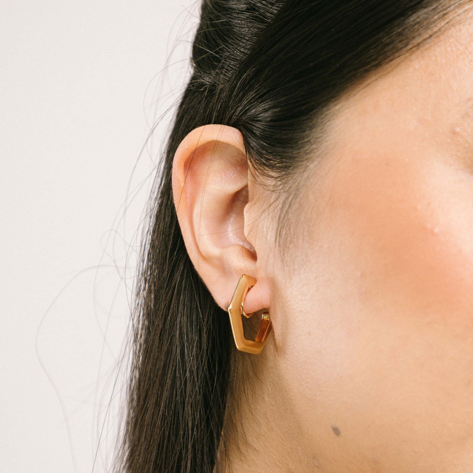 A model wearing our 18k gold plated metal alloy clip-on earrings with non-tarnish, water-resistant coating for durability. Modern hexagon shape with mosquito coil closure and padded backing, adding a timeless classic touch to any ensemble.