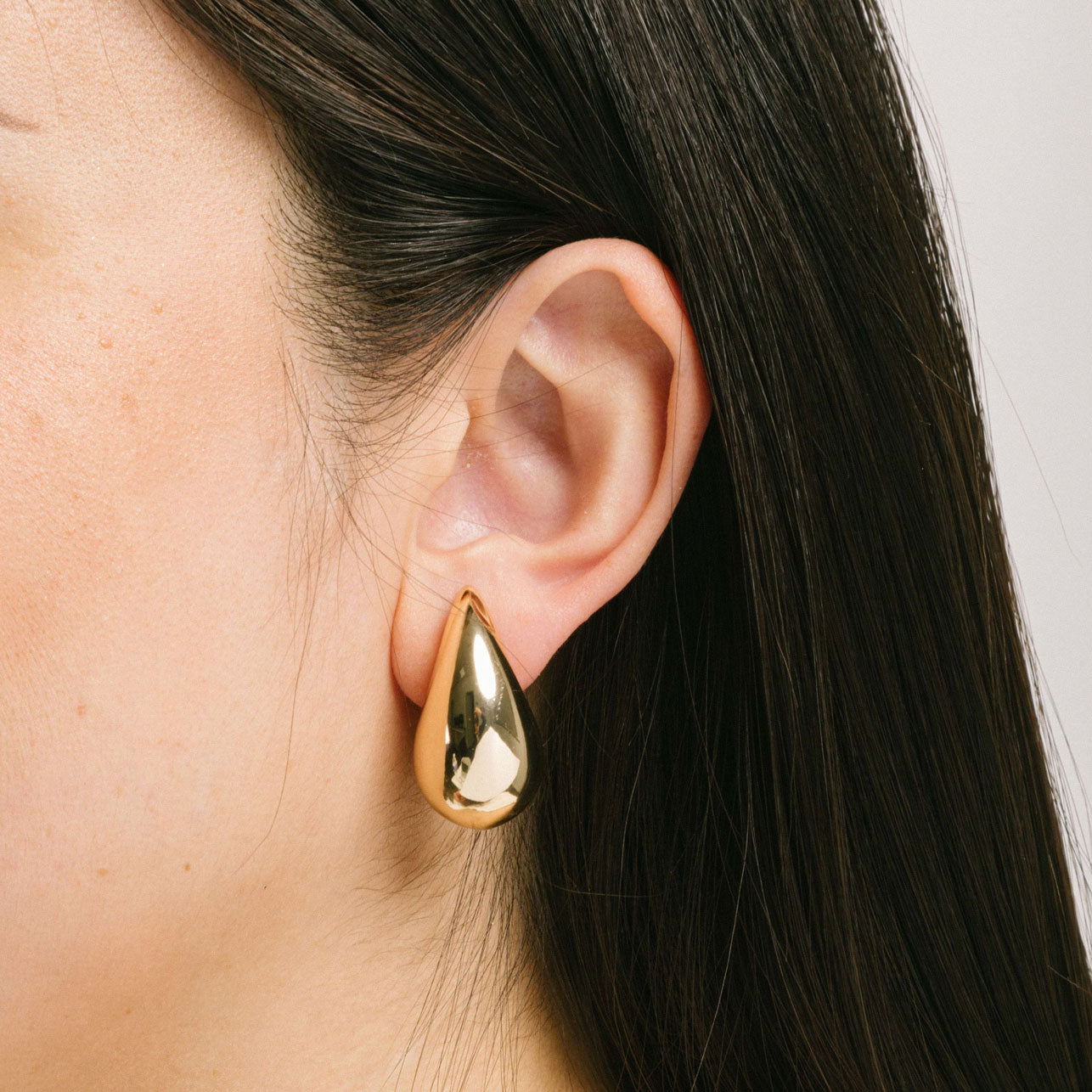 A model wearing the Isla Clip On Earrings in Gold feature a secure screwback closure that fits all ear types, providing an average comfortable wear duration of 8 - 12 hours. The hold strength is strong and you can manually adjust the earrings to your ear size. Constructed of gold toned copper alloy, this item is a single pair.