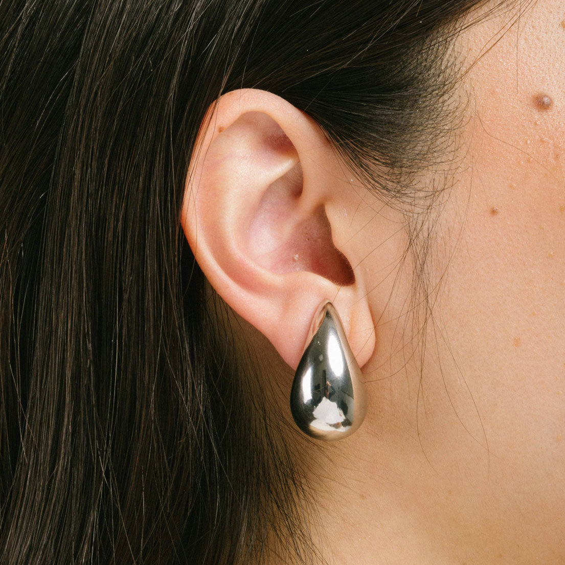 A model wearing the Isla Clip On Earrings in Silver feature a screwback closure that makes them suitable for all ear types, providing a secure hold for up to 12 hours. Easily adjustable, these earrings are constructed with a silver toned copper alloy. Please note: this item is sold as one pair.