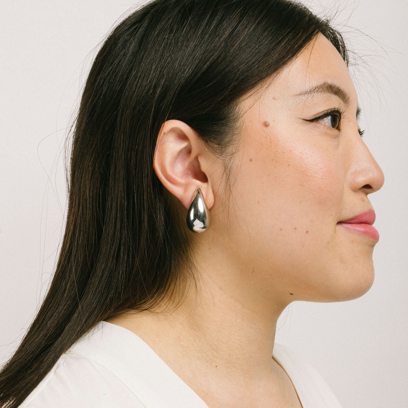 A model wearing the Isla Clip On Earrings in Silver feature a screwback closure that makes them suitable for all ear types, providing a secure hold for up to 12 hours. Easily adjustable, these earrings are constructed with a silver toned copper alloy. Please note: this item is sold as one pair.