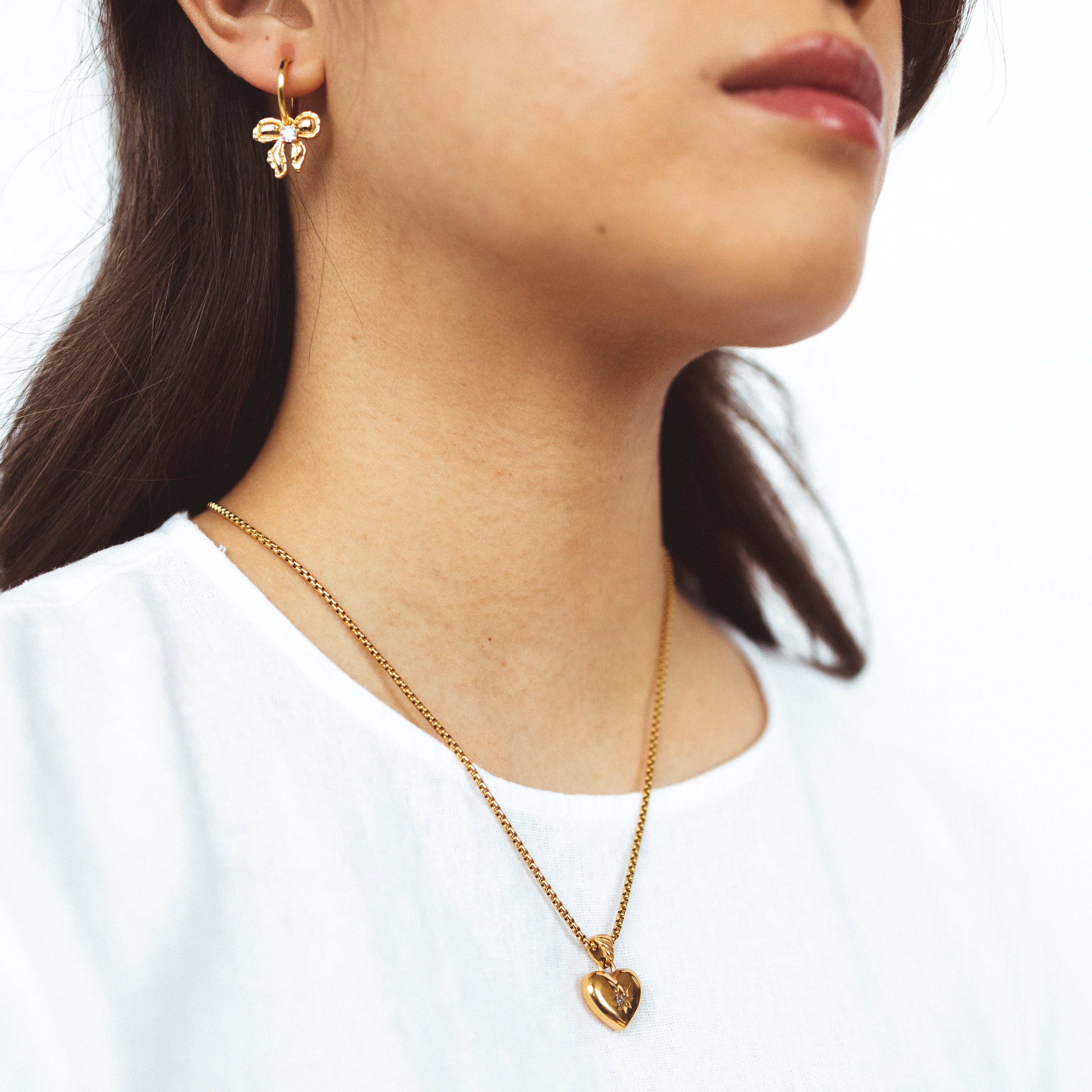 A model wearing the Jude Heart Necklace is expertly crafted from 18K Gold Plated Stainless Steel, resulting in a durable and water-resistant accessory. Its adjustable chain allows for a customized fit. Elegant and functional, this single necklace is a must-have for any jewelry collection.