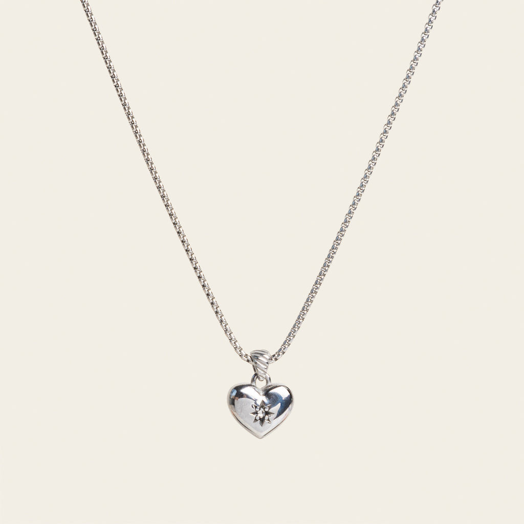 A model wearing the Jude Heart Necklace is expertly crafted from Stainless Steel, resulting in a durable and water-resistant accessory. Its adjustable chain allows for a customized fit. Elegant and functional, this single necklace is a must-have for any jewelry collection.