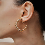 A model wearing the Large Croissant Hoop Clip On Earrings in Gold. These elegant hoops are equipped with a secure screwback closure and adjustable fit to keep them in place all day, even for those with sensitive or keloid prone ears. Enjoy up to 12 hours of comfortable wear in style.