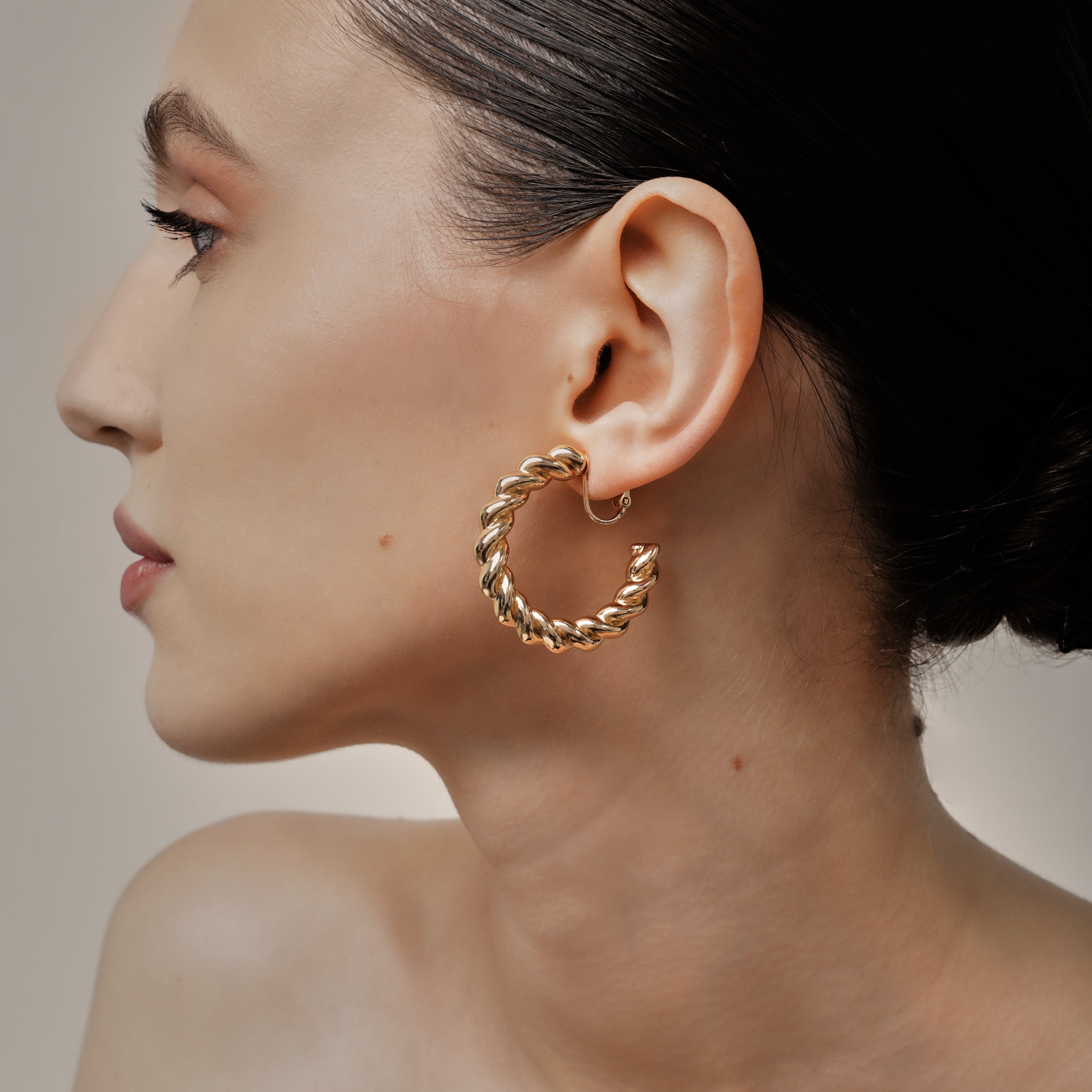 A model wearing the Large Croissant Hoop Clip On Earrings in Gold. These elegant hoops are equipped with a secure screwback closure and adjustable fit to keep them in place all day, even for those with sensitive or keloid prone ears. Enjoy up to 12 hours of comfortable wear in style.