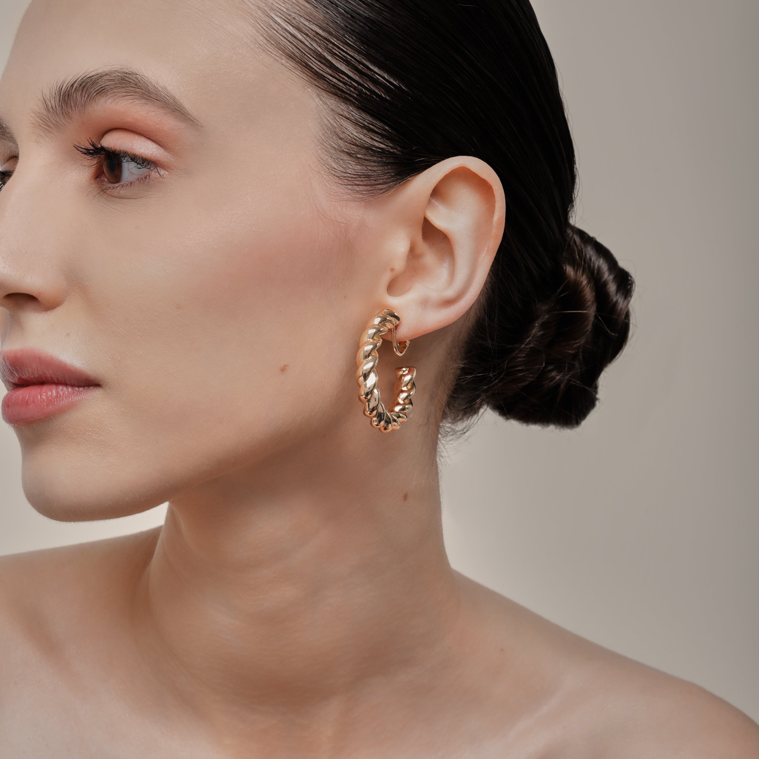 A model wearing the Large Croissant Hoop Clip On Earrings in Gold. These elegant hoops are equipped with a secure screwback closure and adjustable fit to keep them in place all day, even for those with sensitive or keloid prone ears. Enjoy up to 12 hours of comfortable wear in style.