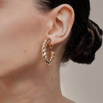 A model wearing the Large Croissant Hoop Clip On Earrings in Gold. These elegant hoops are equipped with a secure screwback closure and adjustable fit to keep them in place all day, even for those with sensitive or keloid prone ears. Enjoy up to 12 hours of comfortable wear in style.