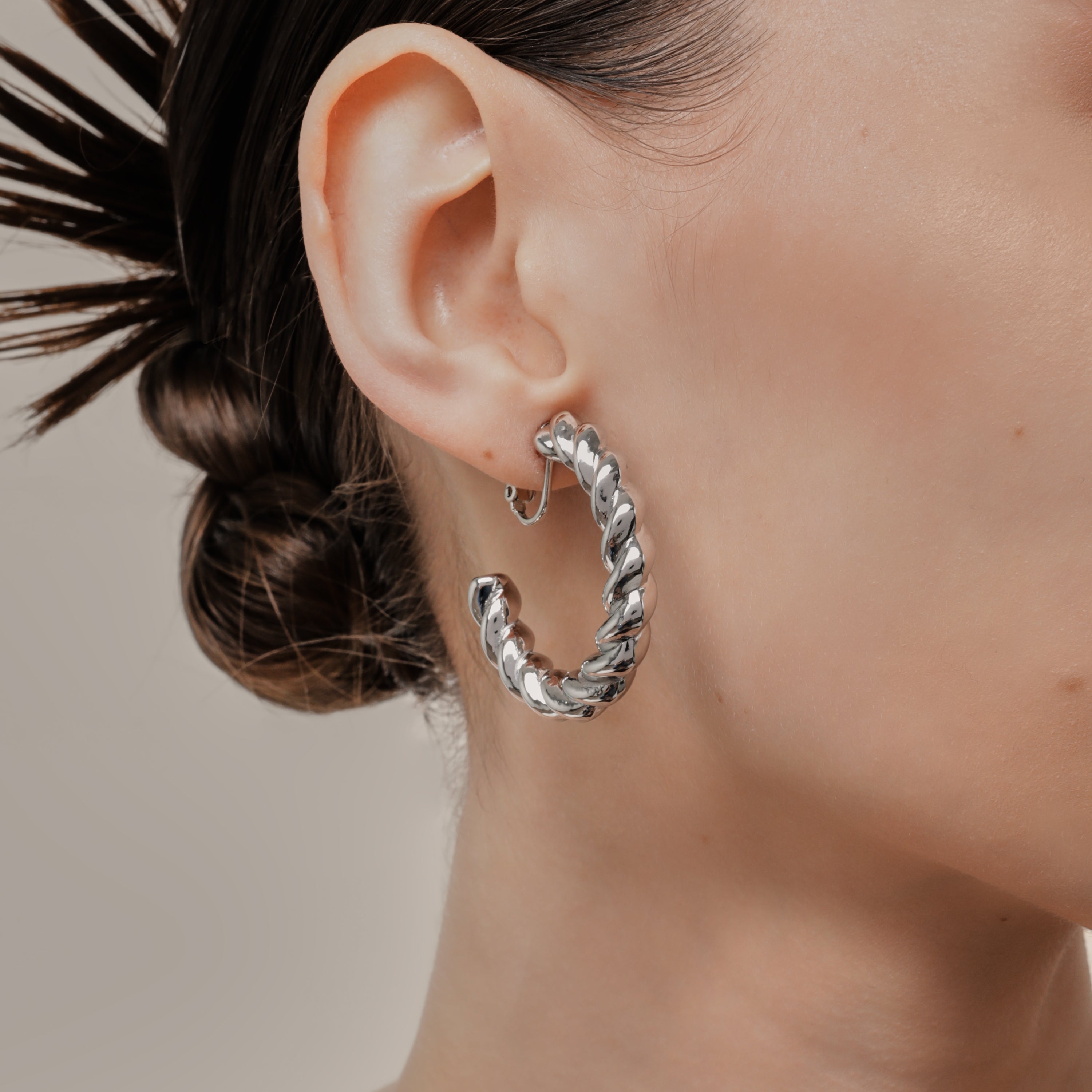 A model wearing the Large Croissant Hoop Clip On Earrings in Silver. These elegant hoops are equipped with a secure screwback closure and adjustable fit to keep them in place all day, even for those with sensitive or keloid prone ears. Enjoy up to 12 hours of comfortable wear in style.