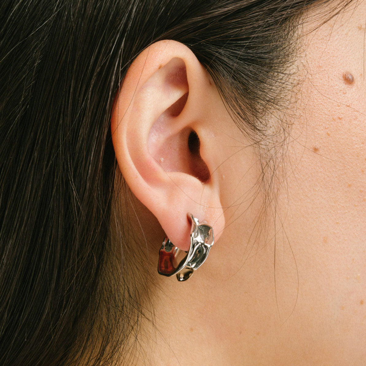 A model wearing the Liquid Melt Hoop Clip On Earrings feature a Mosquito Coil Clip-On closure ideal for all ear types including thick/large ears, sensitive ears, small/thin ears, and stretched/healing ears. On average, they offer a comfortable wear duration of 24 hours and a medium secure hold, with an adjustable fit. Crafted from silver toned copper alloy, each purchase includes one pair of the earrings.