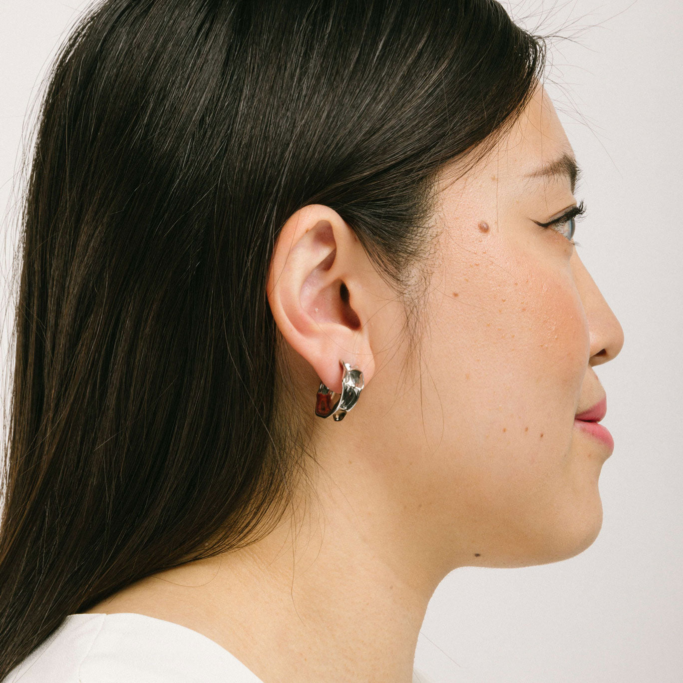 A model wearing the Liquid Melt Hoop Clip On Earrings feature a Mosquito Coil Clip-On closure ideal for all ear types including thick/large ears, sensitive ears, small/thin ears, and stretched/healing ears. On average, they offer a comfortable wear duration of 24 hours and a medium secure hold, with an adjustable fit. Crafted from silver toned copper alloy, each purchase includes one pair of the earrings.