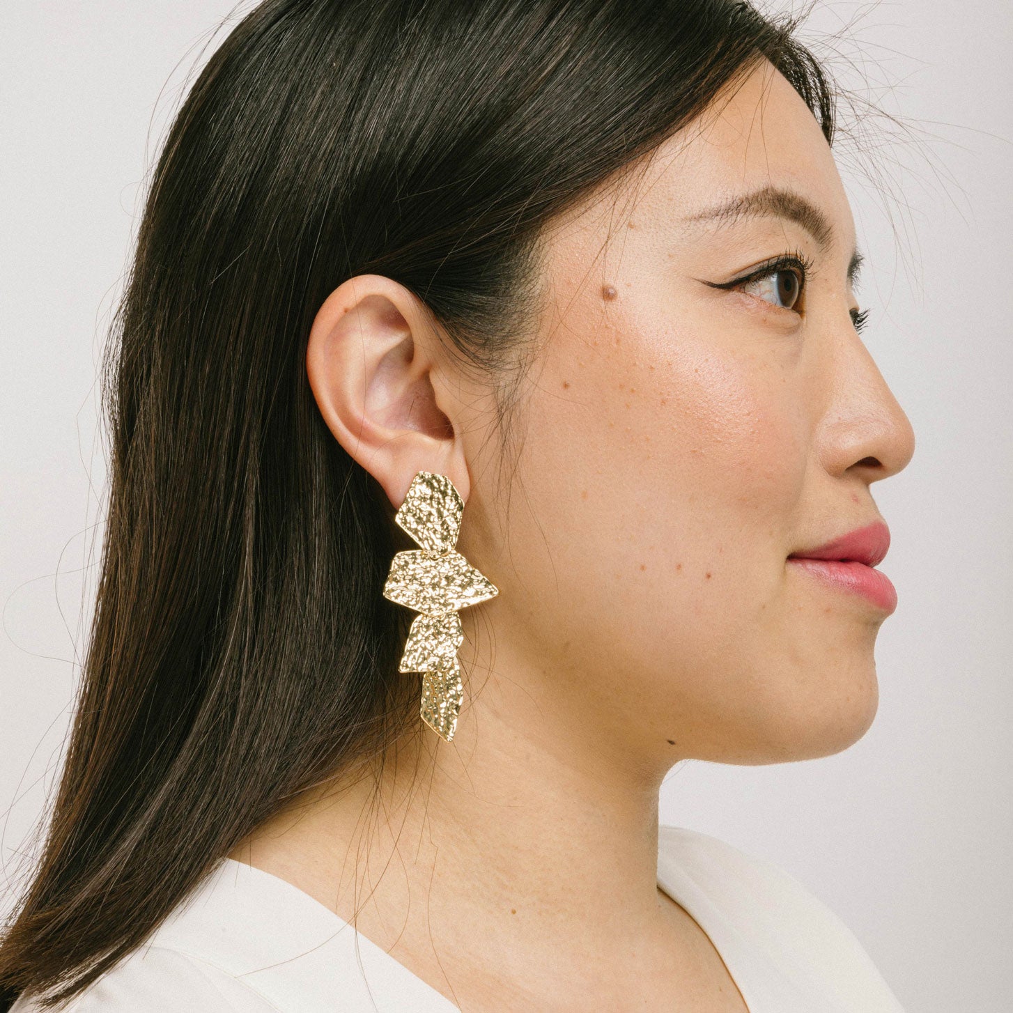 A model wearing the Manhattan Drop Clip On Earrings in Gold provide a secure and comfortable fit for any ear type. The padded clip-on design features a zinc and copper alloy construction, and lasts approximately 8-12 hours. As the earring pairs are non-adjustable, each purchase contains a single pair.