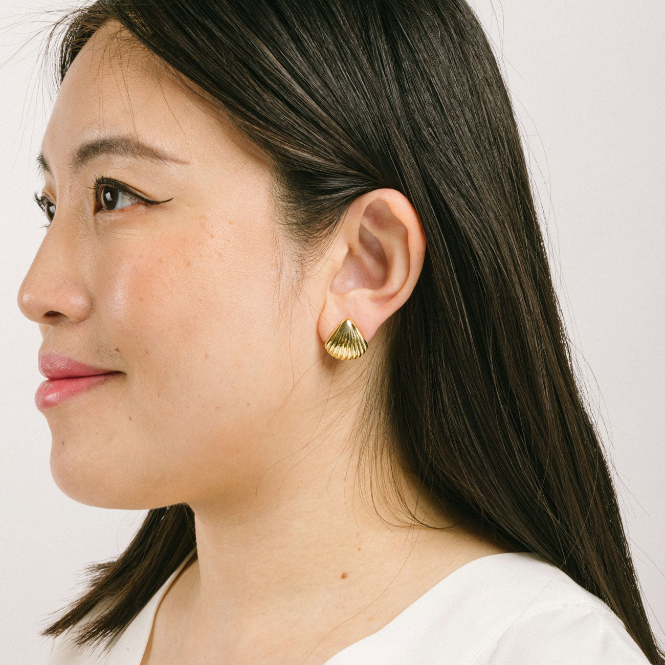 A model wearing the Mer Clip On earrings feature an easy-to-use mosquito coil clip-on closure, designed for all ear types including thick/large ears, sensitive ears, small/thin ears, and stretched/healing ears. Enjoy a comfortable wear duration lasting up to 24 hours with a medium secure hold. Easily adjust the padding forward once it’s on the ear. Crafted with gold-toned copper alloy, each package contains one pair.