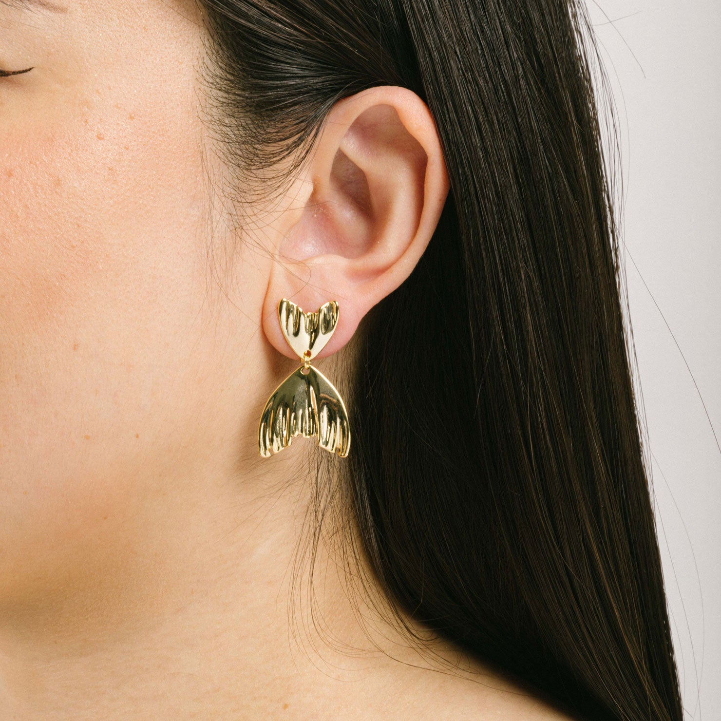 A model wearing the Mermaid Tail Clip On Earrings in Gold are perfect for all ear types including thick/large ears, sensitive ears, small/thin ears, and stretched/healing ears. With a zinc alloy body, these earrings offer a secure hold of up to 8-12 hours and come with removable rubber padding. Please note, item is only one pair.