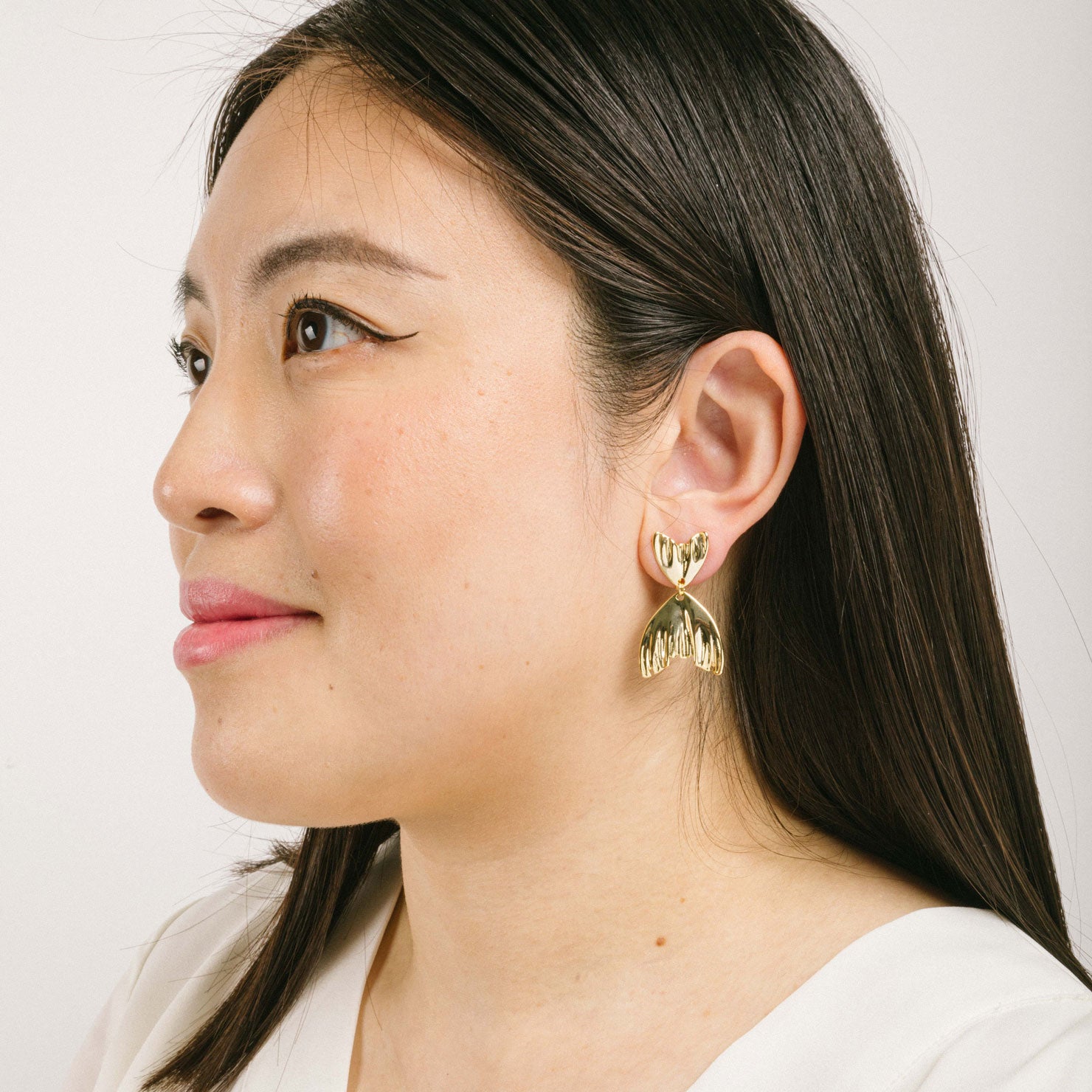 A model wearing the Mermaid Tail Clip On Earrings in Gold are perfect for all ear types including thick/large ears, sensitive ears, small/thin ears, and stretched/healing ears. With a zinc alloy body, these earrings offer a secure hold of up to 8-12 hours and come with removable rubber padding. Please note, item is only one pair.