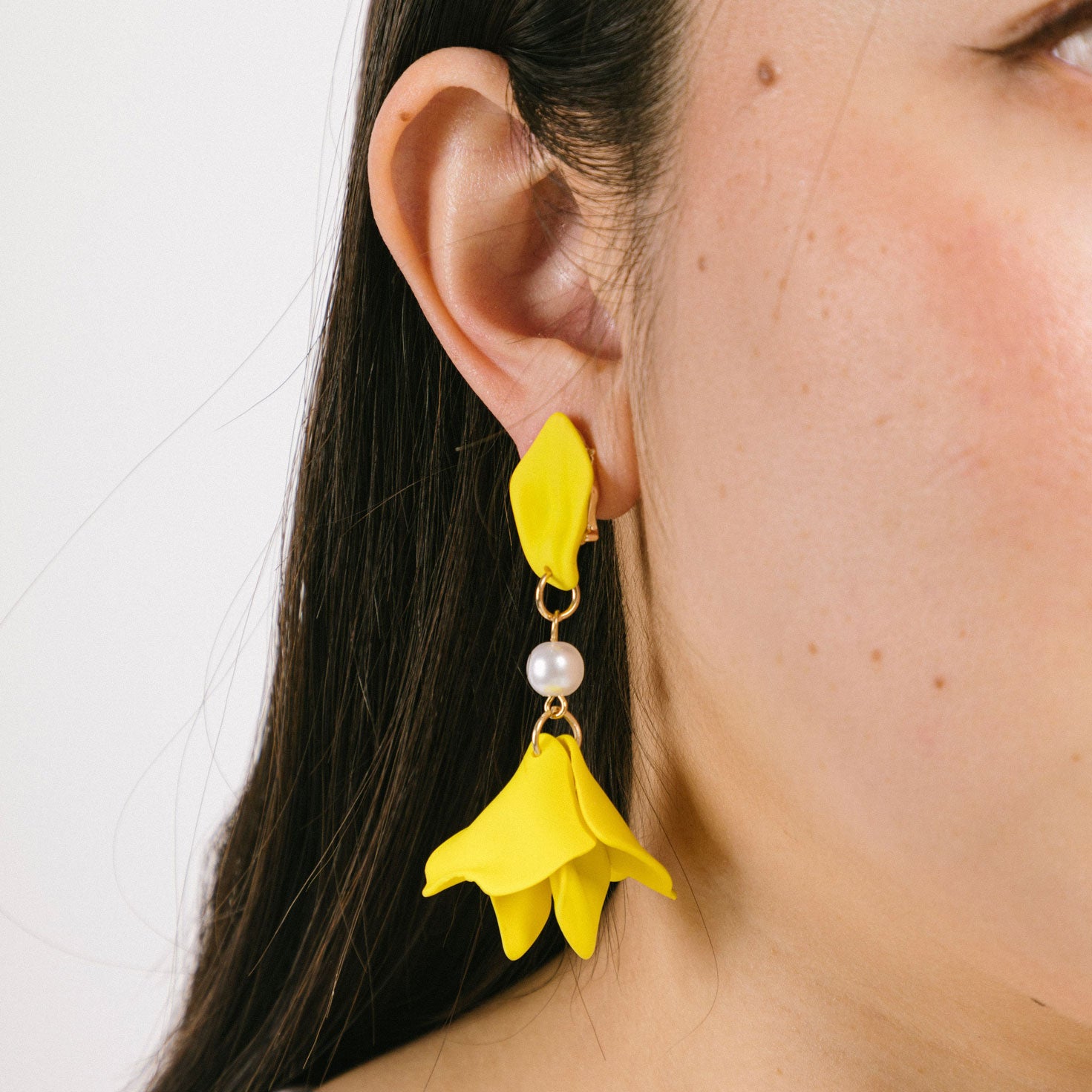 A model wearing the Metallic Petal Clip On Earrings feature a secure, padded clip-on closure for comfortable wear. Suitable for all ear types, they hold strong for up to 12 hours and have a simulated pearl finish. Each order comes with one pair. Materials include acrylic and simulated pearl. Clips feature removable rubber padding.