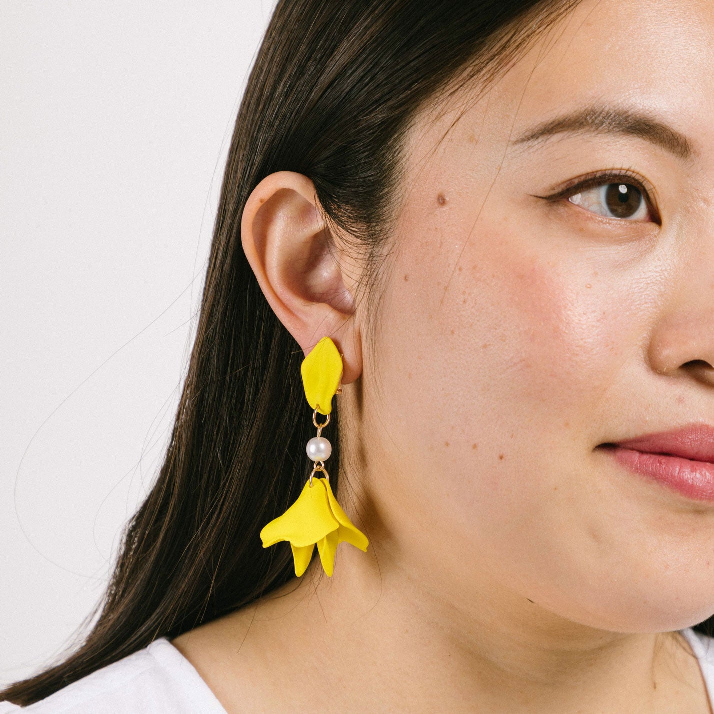 A model wearing the Metallic Petal Clip On Earrings feature a secure, padded clip-on closure for comfortable wear. Suitable for all ear types, they hold strong for up to 12 hours and have a simulated pearl finish. Each order comes with one pair. Materials include acrylic and simulated pearl. Clips feature removable rubber padding.