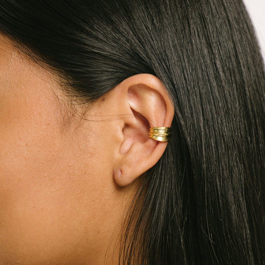 A model wearing the Mona Ear Cuff in Gold is an ideal piece for all ear types. Made from 18K gold-plated 925 sterling silver, it features a medium-secure hold and allows for gentle adjustment. Thanks to its non-tarnish and water-resistant properties, it can be comfortably worn for up to 24 hours. One piece.