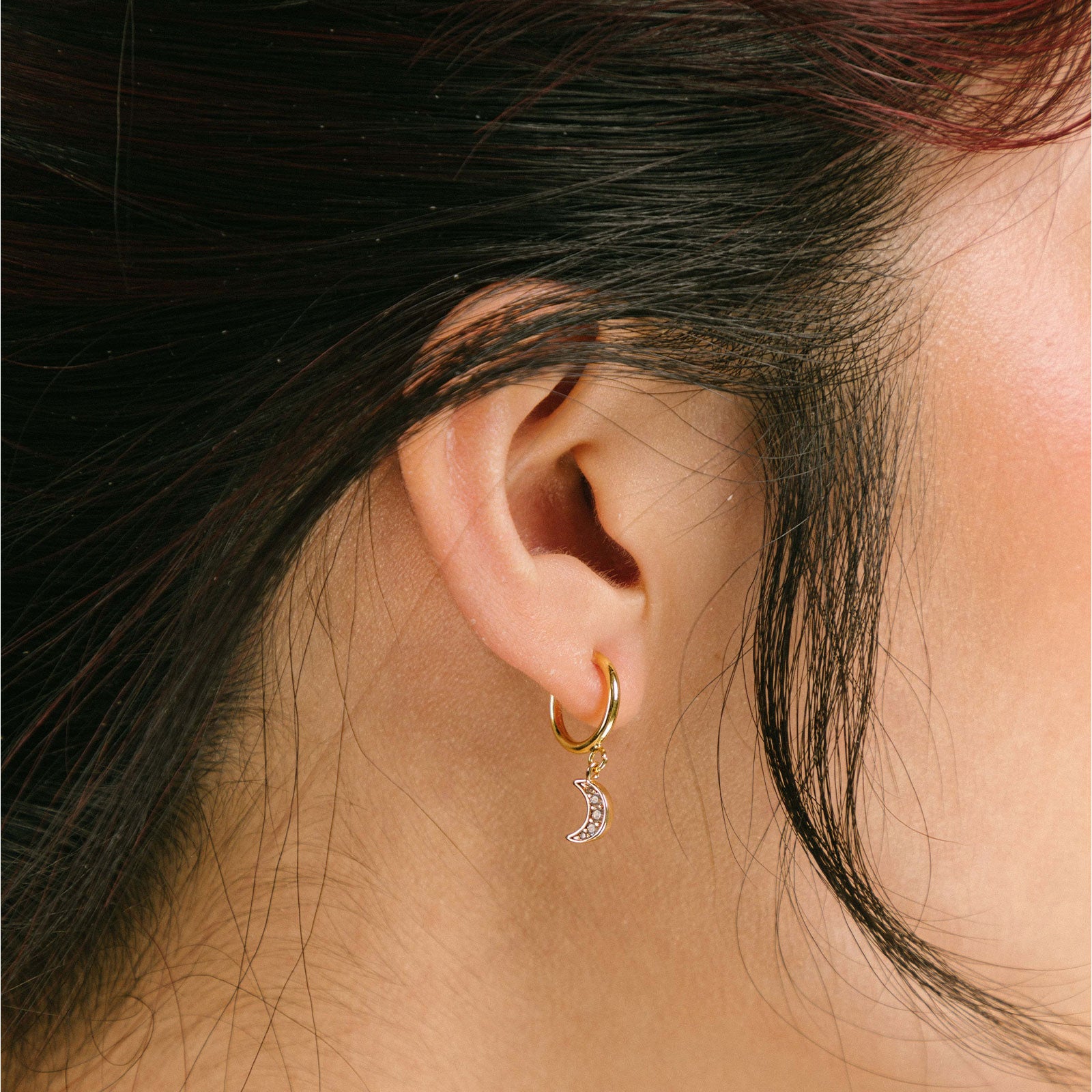 A model wearing the Moon Charm Clip on Earrings feature a sliding spring closure type, specifically designed for those with small or thinner ear lobes. This type of closure ensures a very secure hold and an adjustable fit to accommodate different ear thicknesses. Sold as a single pair, these earrings are crafted from brass and feature cubic zirconia details. Typically suitable for wear of 2-4 hours.
