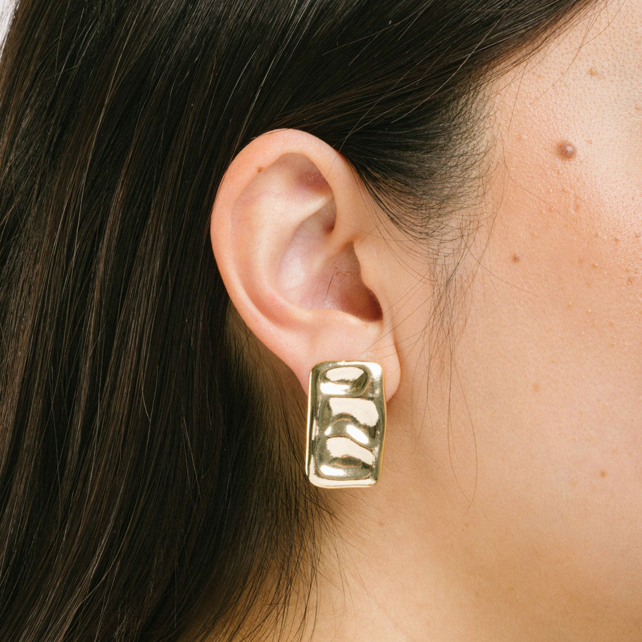 A model wearing the Nova Clip On Earrings in Gold feature a secure and comfortable padded clip-on design, suitable for all ear types. The earrings are crafted with Gold Tone Copper Alloy and offer an average comfortable wear duration of 8-12 hours. The design of the earring does not allow for adjustment, and each item sold is a single pair.