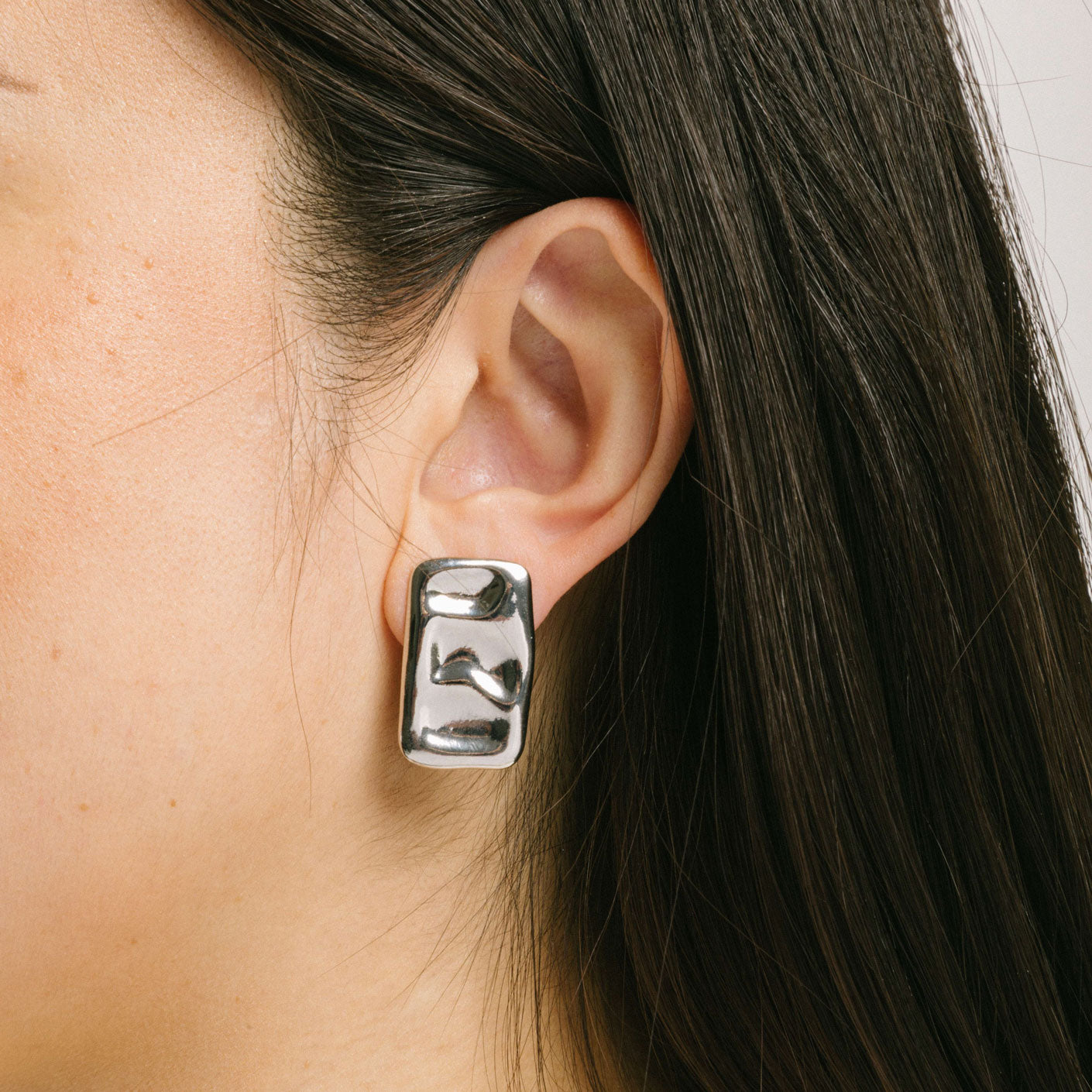 A model wearing the Nova Clip On Earrings in Silver feature a padded clip-on closure and are suitable for all ear types, including thick/large ears, thin/small ears, and even ears that are healing or stretched. Expect a secure and comfortable hold for 8 - 12 hours. Crafted using a silver tone copper alloy, this piece contains one pair of removable rubber-padded clip-on earrings.