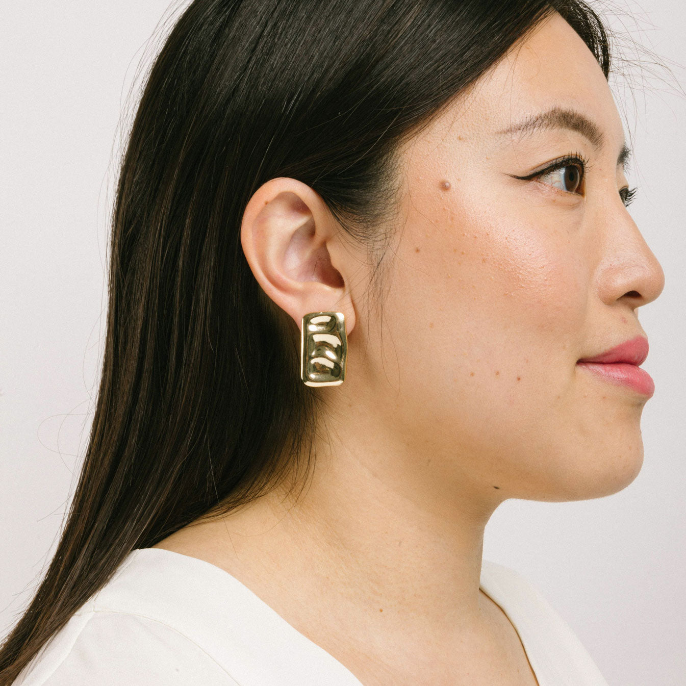 A model wearing the Nova Clip On Earrings in Gold feature a secure and comfortable padded clip-on design, suitable for all ear types. The earrings are crafted with Gold Tone Copper Alloy and offer an average comfortable wear duration of 8-12 hours. The design of the earring does not allow for adjustment, and each item sold is a single pair.