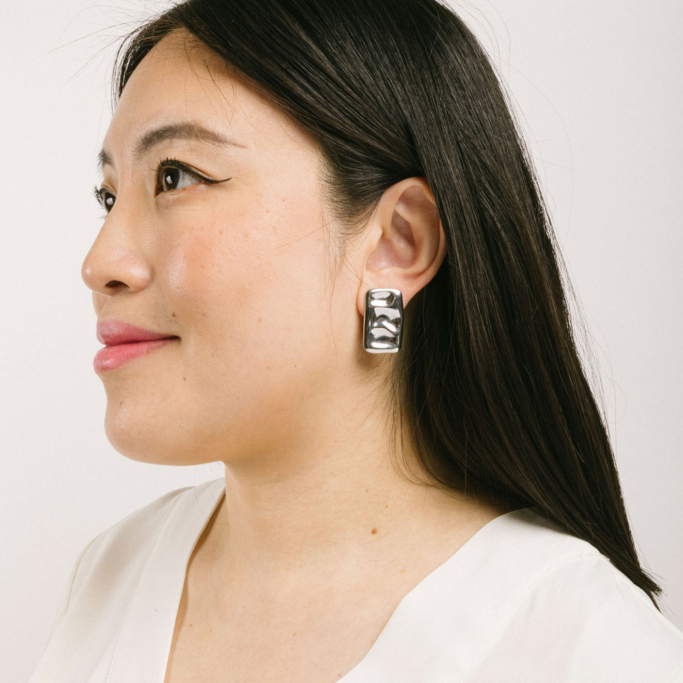A model wearing the Nova Clip On Earrings in Silver feature a padded clip-on closure and are suitable for all ear types, including thick/large ears, thin/small ears, and even ears that are healing or stretched. Expect a secure and comfortable hold for 8 - 12 hours. Crafted using a silver tone copper alloy, this piece contains one pair of removable rubber-padded clip-on earrings.